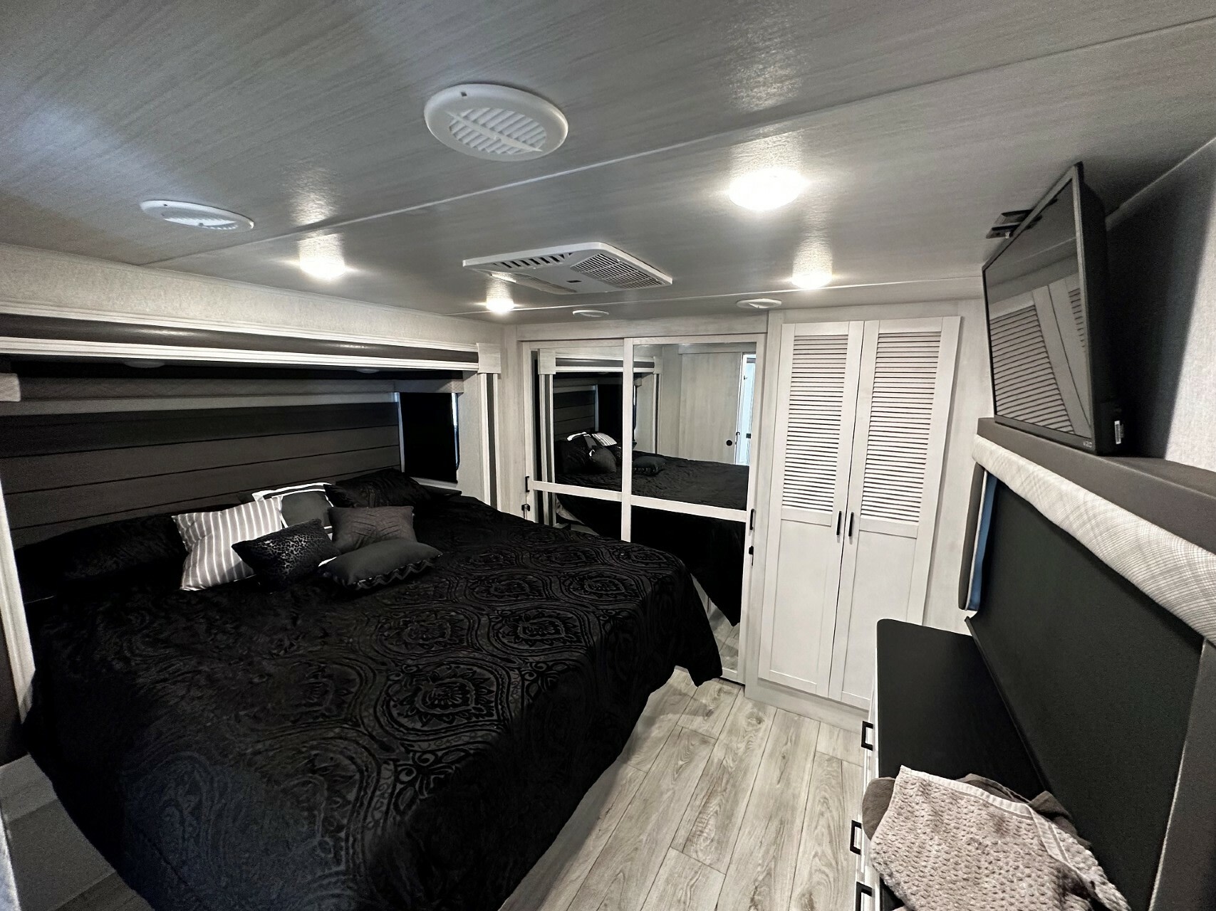 Modern RV rental bedroom featuring a large black bed, mirrored closets, and a mounted TV.. East To West Ahara 2023