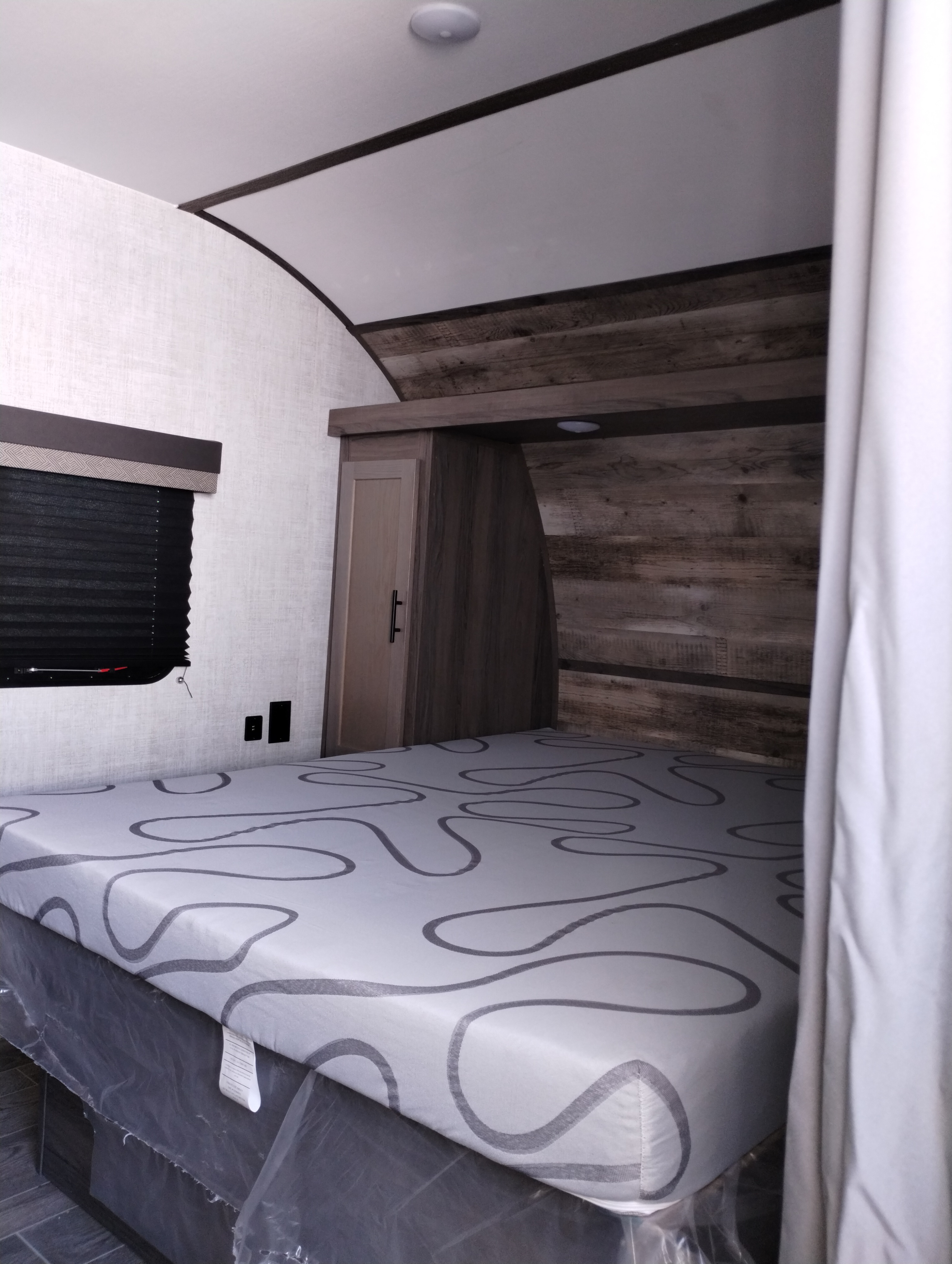 Cozy RV rental bedroom featuring a patterned mattress, window with black blinds, wood walls, and built-in storage.. Gulf Stream Ameri-Lite 2022