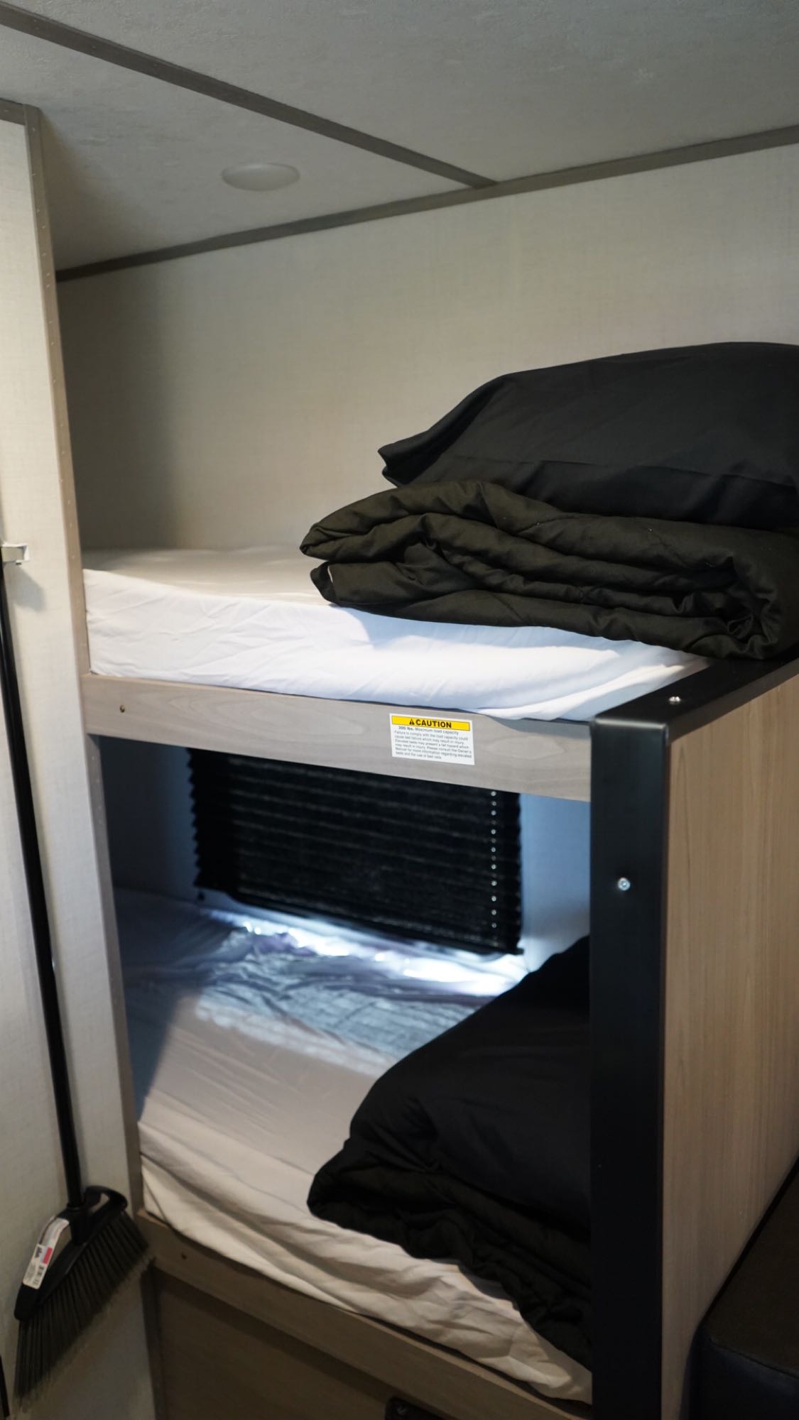 Inside an RV rental: two bunk beds with white sheets, black bedding, and a privacy shade between them.. Dutchmen Coleman Lantern LT 2023