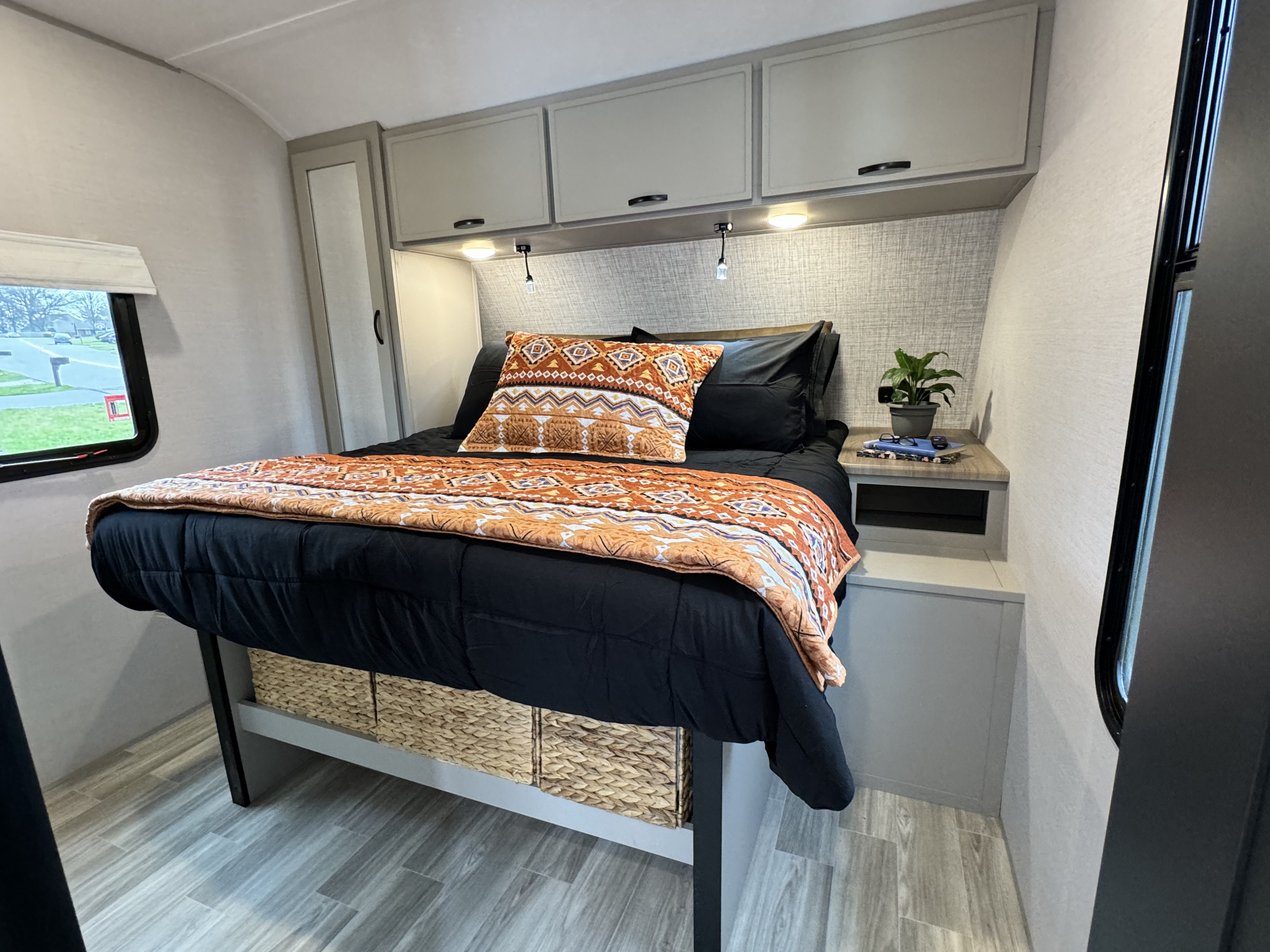 Modern RV rental bedroom with patterned bedding, overhead cabinets, and practical woven under-bed storage. Ideal for trips.. Forest River Vibe 34BH 2024