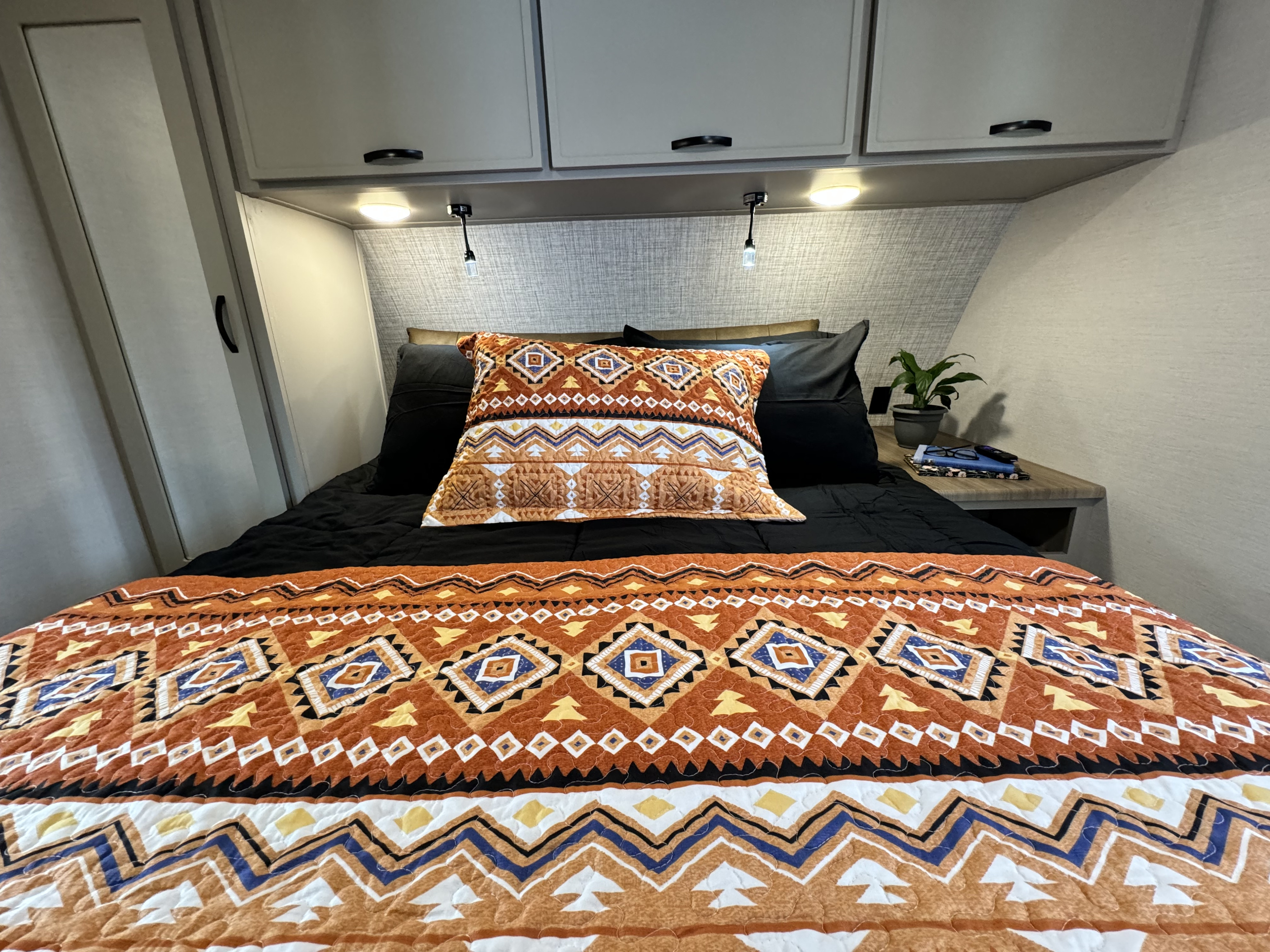 Experience cozy comfort in this RV rental bedroom, featuring a vibrant Southwestern quilt, ample storage, and reading lights.. Forest River Vibe 34BH 2024
