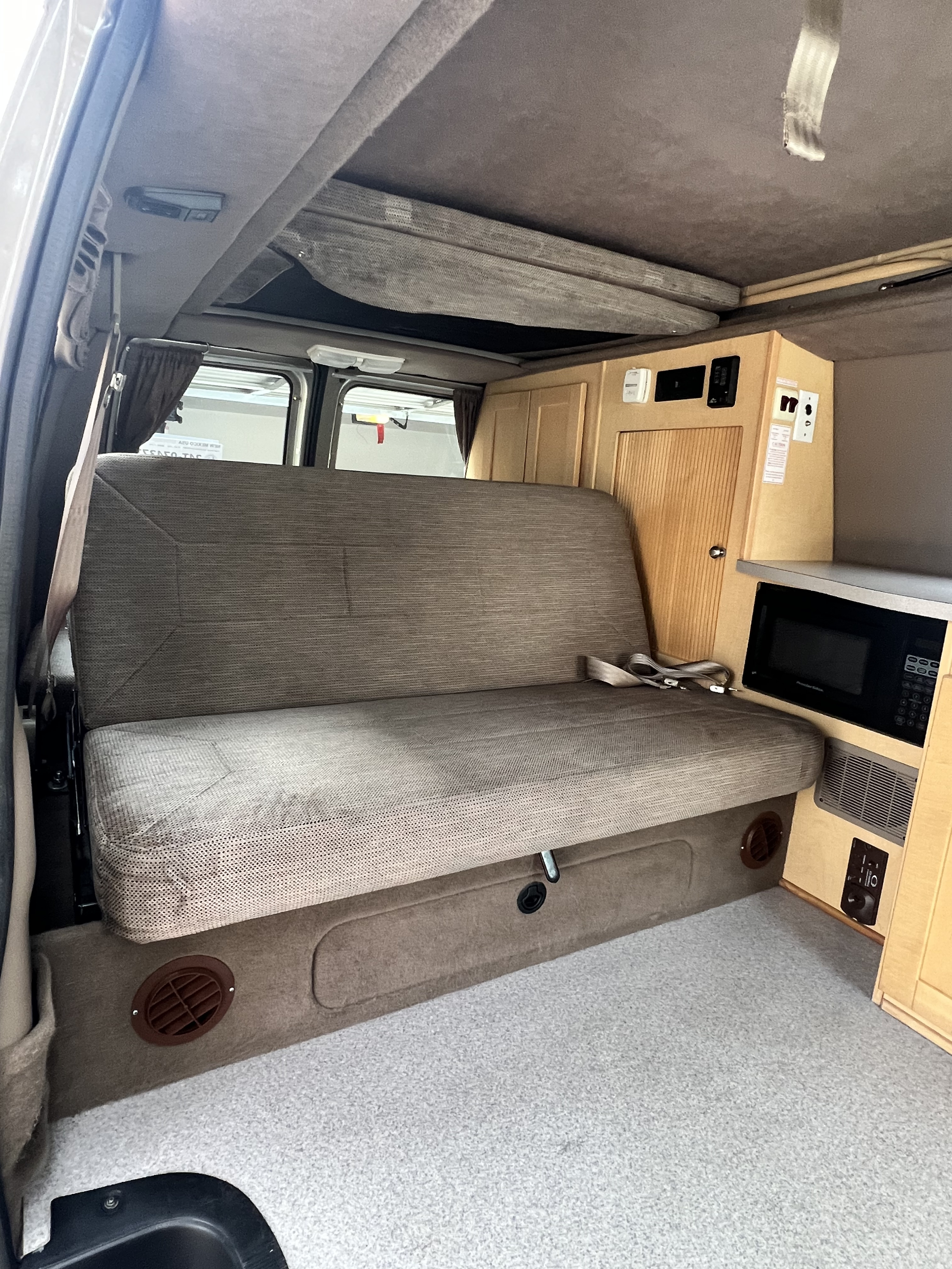 Interior of a practical rv rental with a large bench seat, overhead bunk, and built-in kitchenette including a microwave.. Ford Pleasure Way Xl Rd Widebody 2002