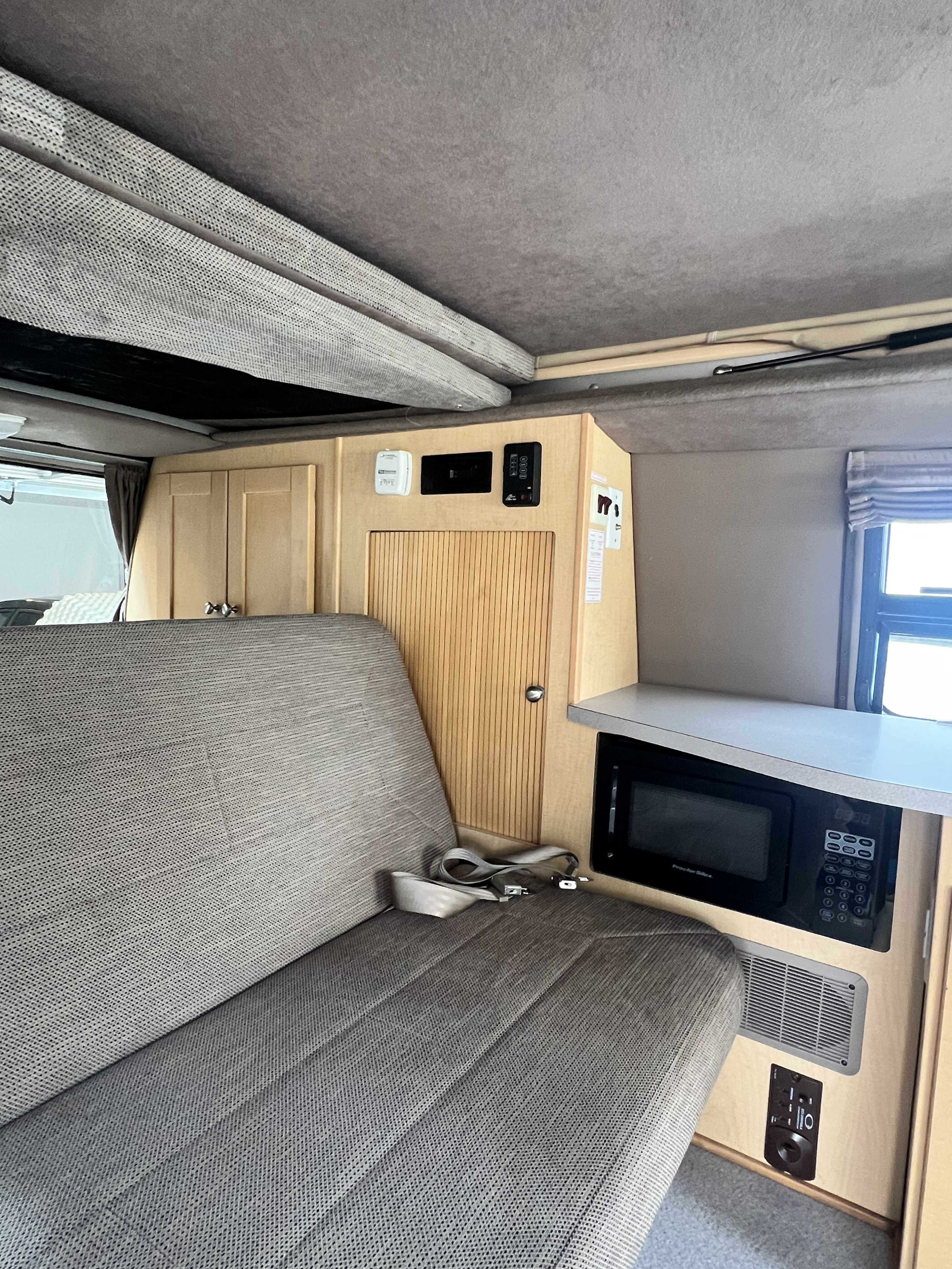 RV rental: Pop-up camper interior with bench seat, microwave, and wood storage. Functional living space.. Ford Pleasure Way Xl Rd Widebody 2002