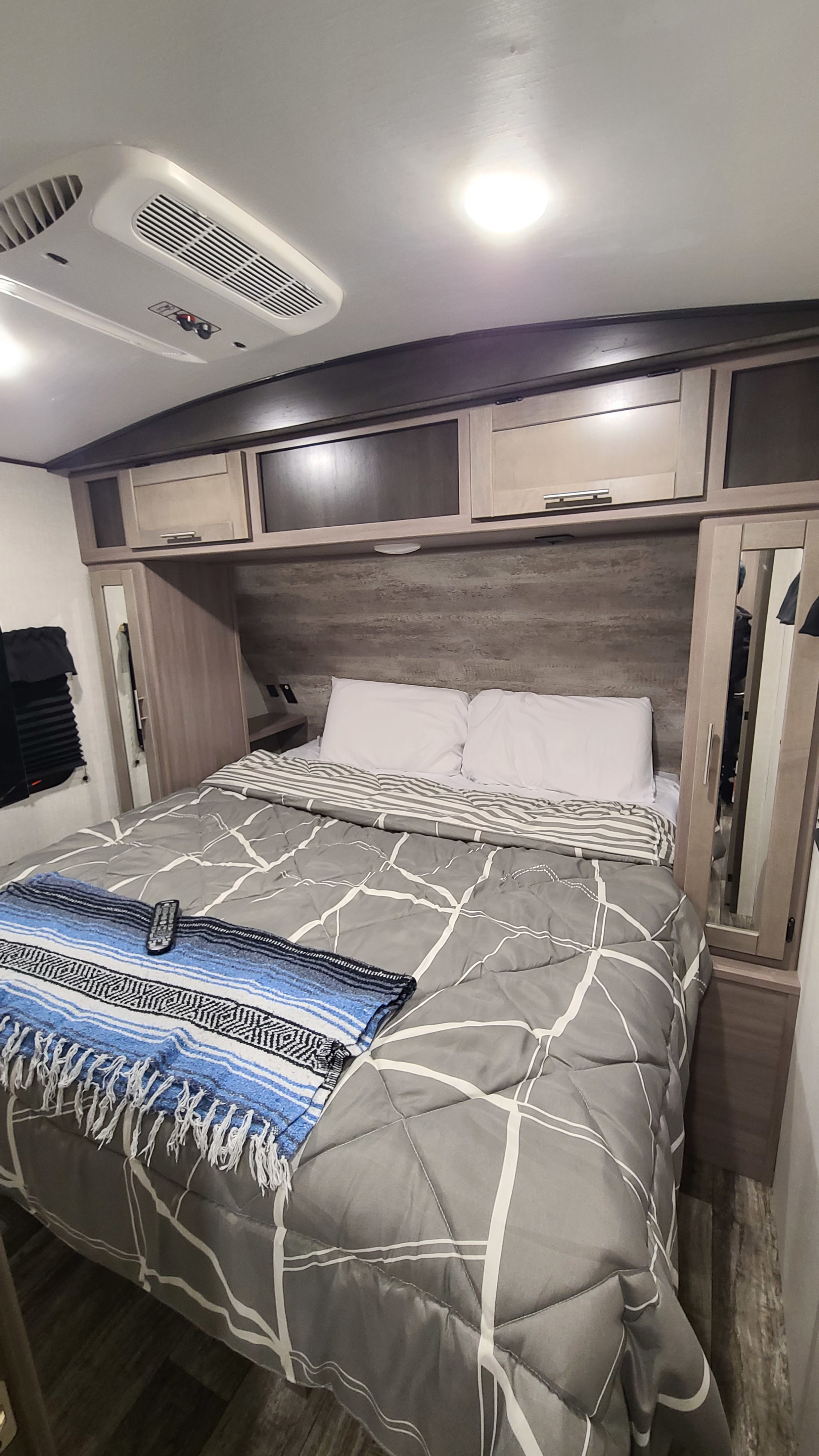 View inside an RV rental's cozy bedroom, showcasing a bed with gray comforter, white pillows, and overhead storage/AC unit.. Crossroads RV Sunset Trail Super Lite 2022
