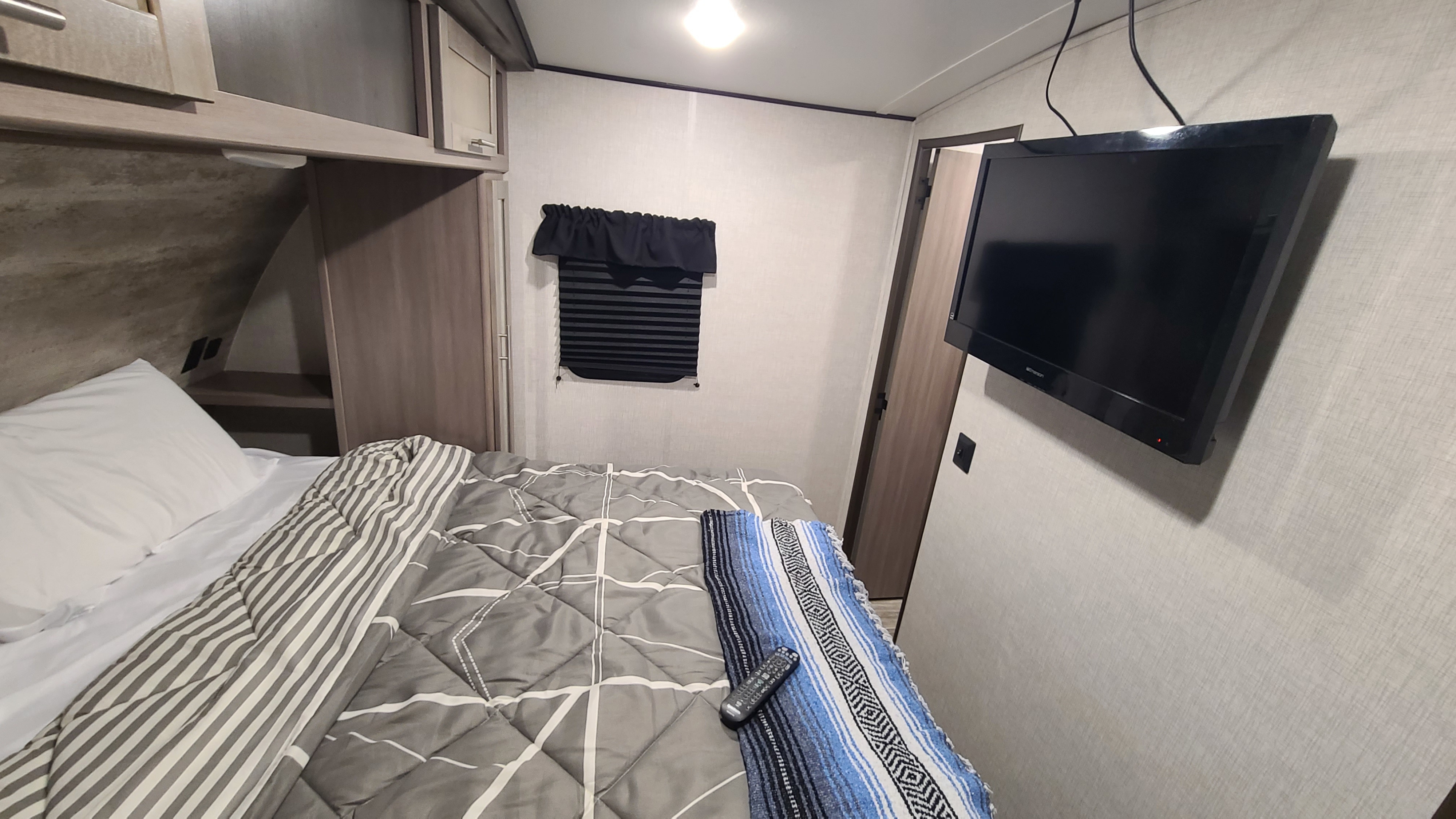 Cozy RV rental bedroom showing a bed with patterned bedding, wall-mounted TV, and window. Ideal for travel.. Crossroads RV Sunset Trail Super Lite 2022