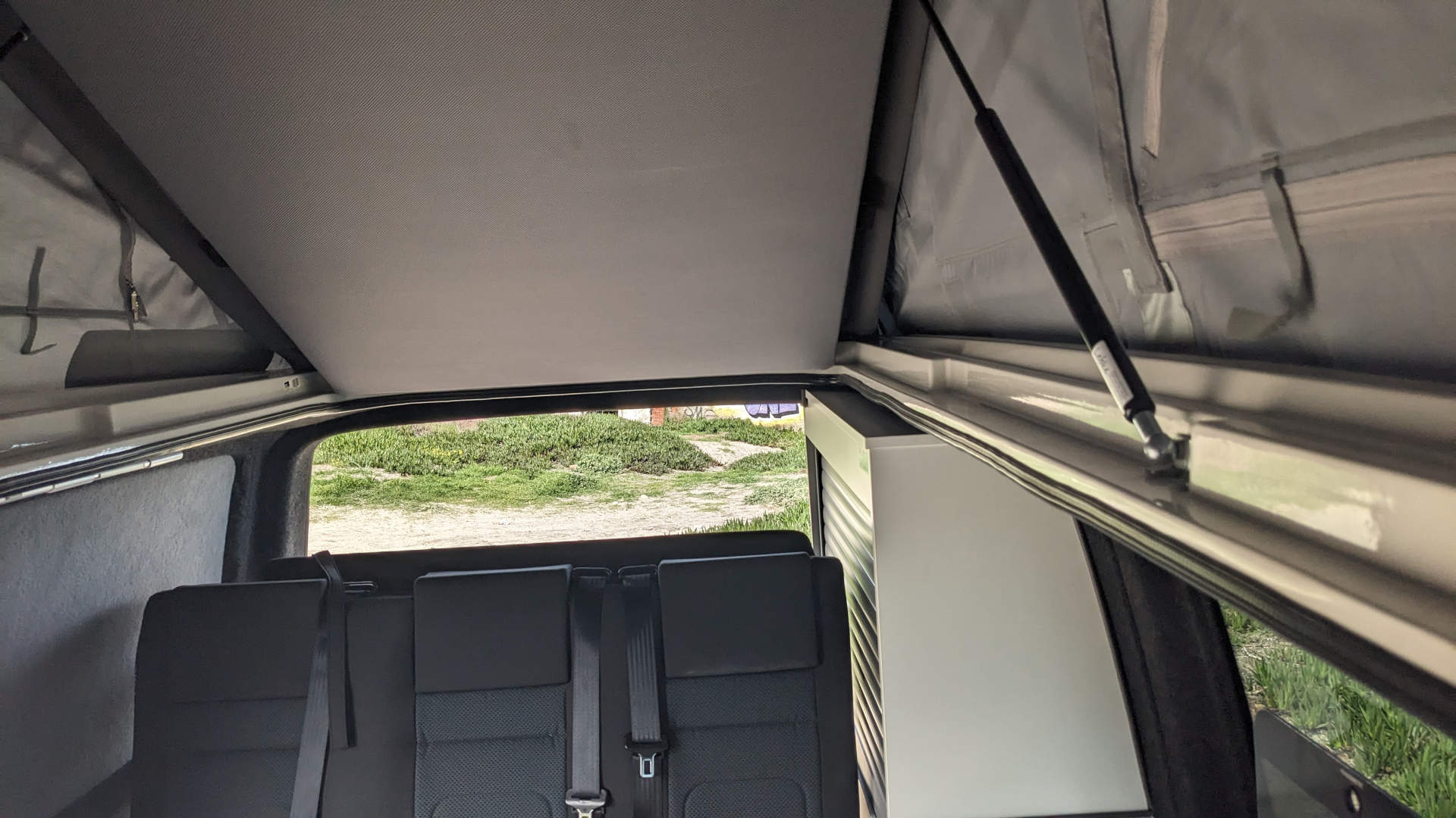 Inside an RV rental, the rear seats offer a view of the outdoors through the back window, beneath a raised pop-top roof.. Volkswagen T6 transporter 2019