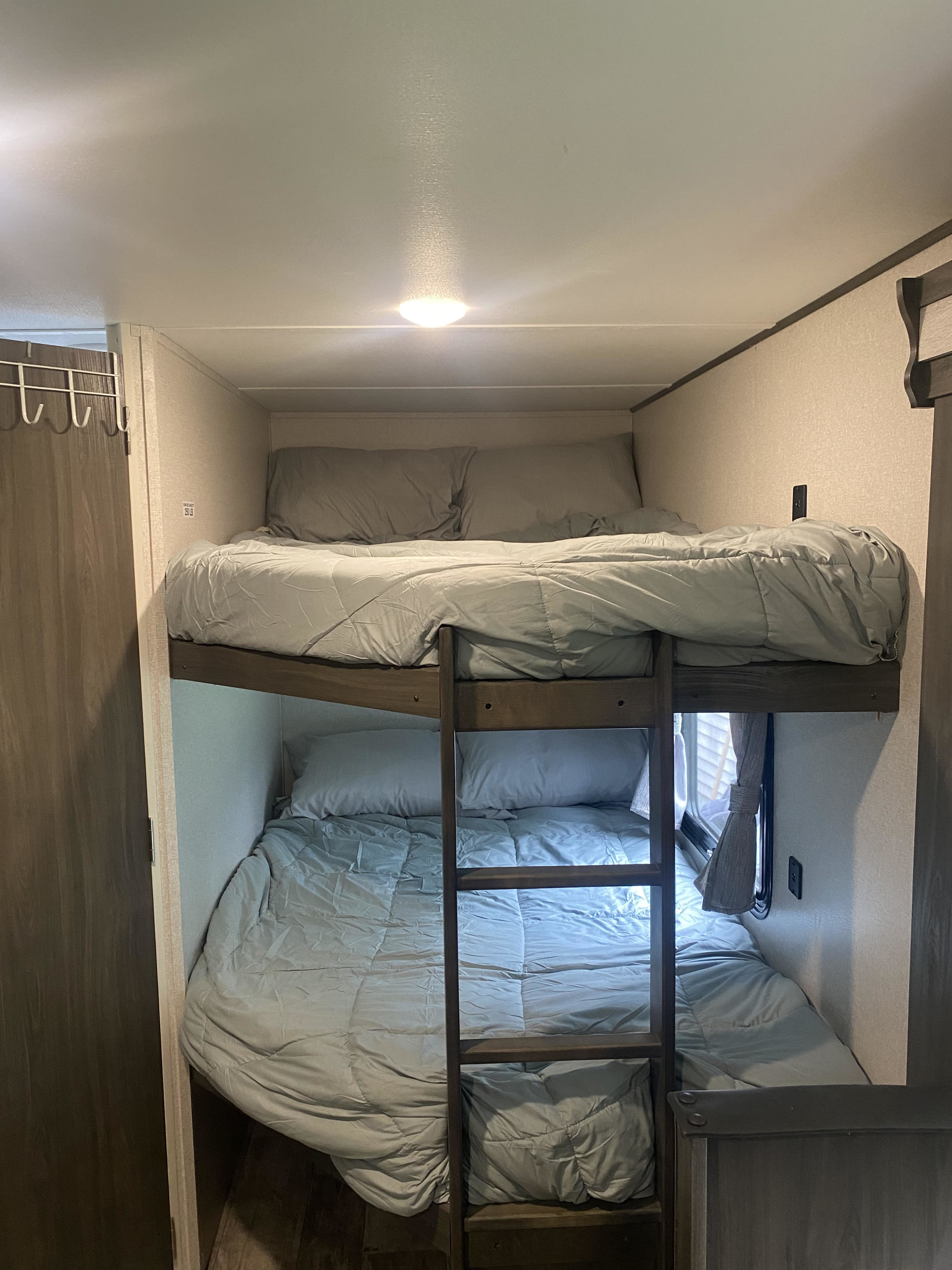 Inside an RV rental, showing comfortable bunk beds with gray bedding and a ladder for compact sleeping.. Forest River Shasta 2021