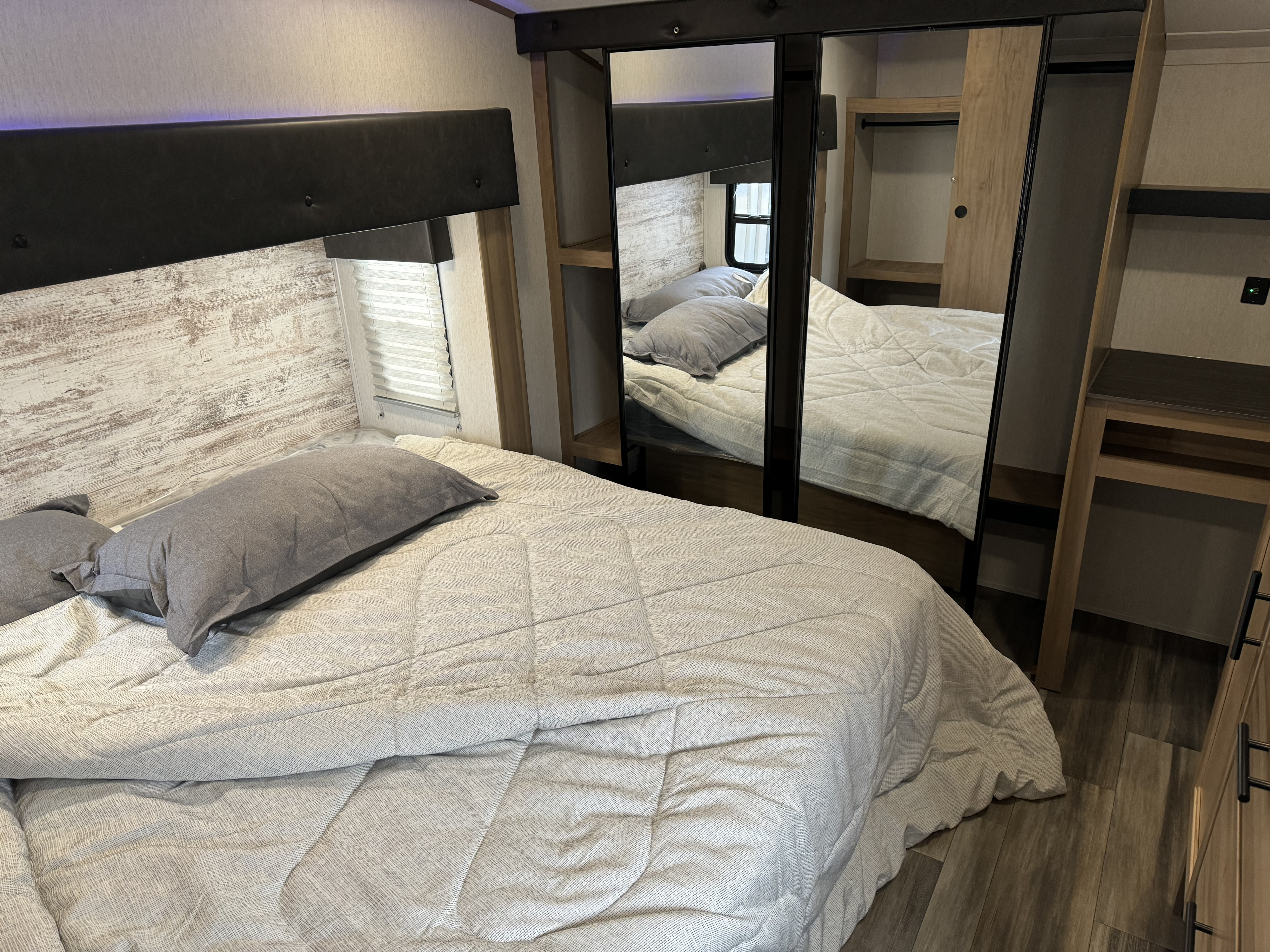 Inviting RV rental bedroom with a bed, grey comforter, mirrored wardrobe, window, and distressed wood-look wall.. Forest River Cherokee Arctic Wolf 2023