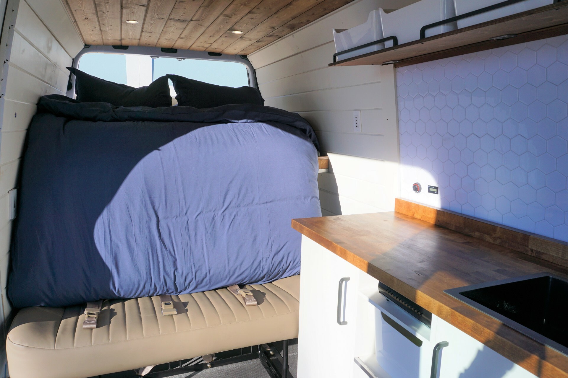 RV rental interior: Comfy bed over belted bench, wood counter, sink, and hex tile kitchen backsplash.. Mercedes-Benz Sprinter 2020