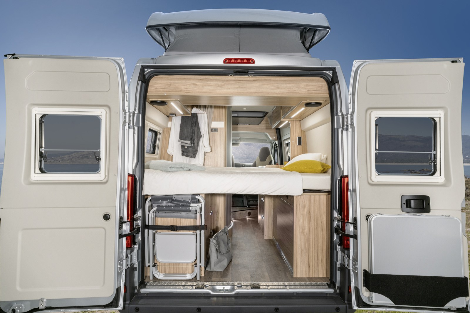 Rear view of a spacious RV rental interior with bed, storage, and open doors showing a scenic landscape.. Hymer Ayers Rock 2024