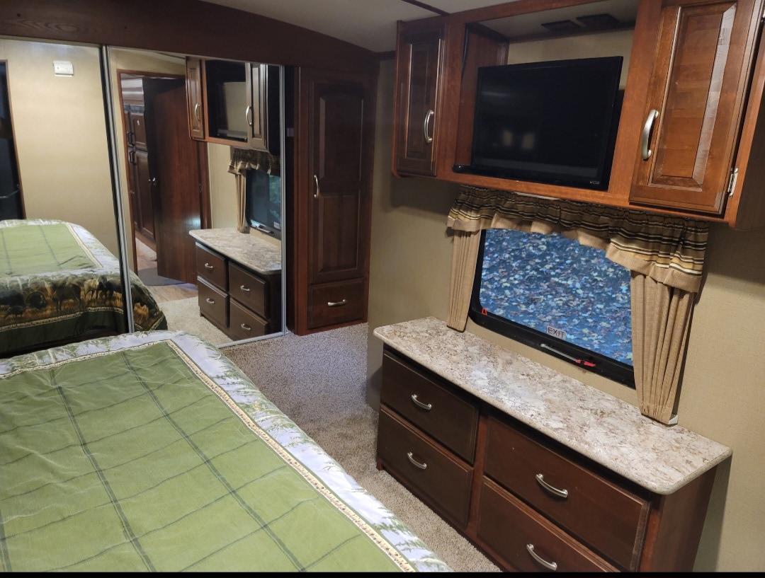 Experience comfort in this RV rental bedroom: bed, mirrored closet, dresser, TV, and window views await.. Keystone RV Outback Super-Lite 2015