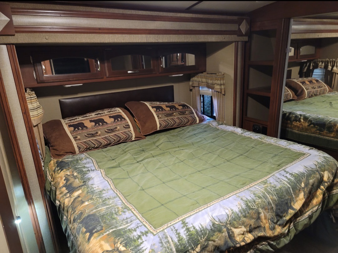 Cozy RV rental bedroom with a large bed, rustic wildlife bedding, overhead cabinets, and a mirrored closet.. Keystone RV Outback Super-Lite 2015