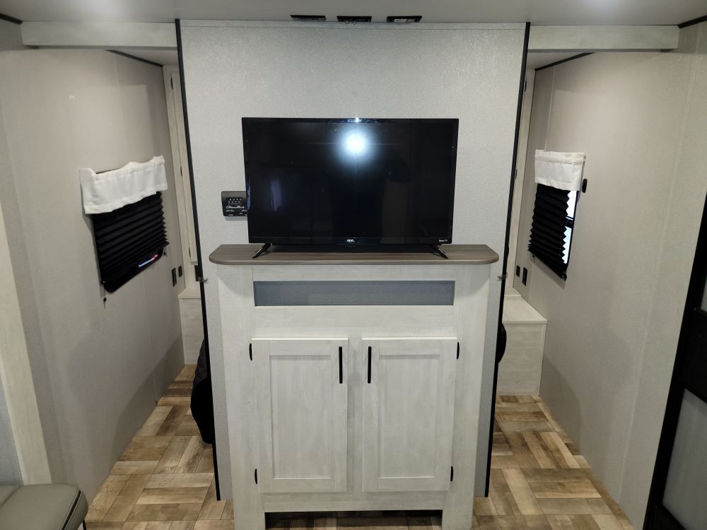 RV rental interior showing a central TV console atop light-colored cabinets, flanked by two narrow passages to sleeping areas.. Forest River Shasta 2022
