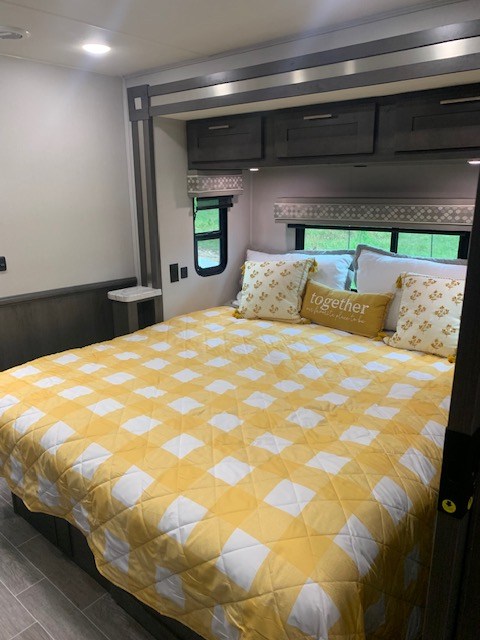 Experience comfort in this cozy RV rental bedroom. Features a large bed with a bright yellow checkered quilt, pillows, and overhead storage.. Georgetown GT5 2023