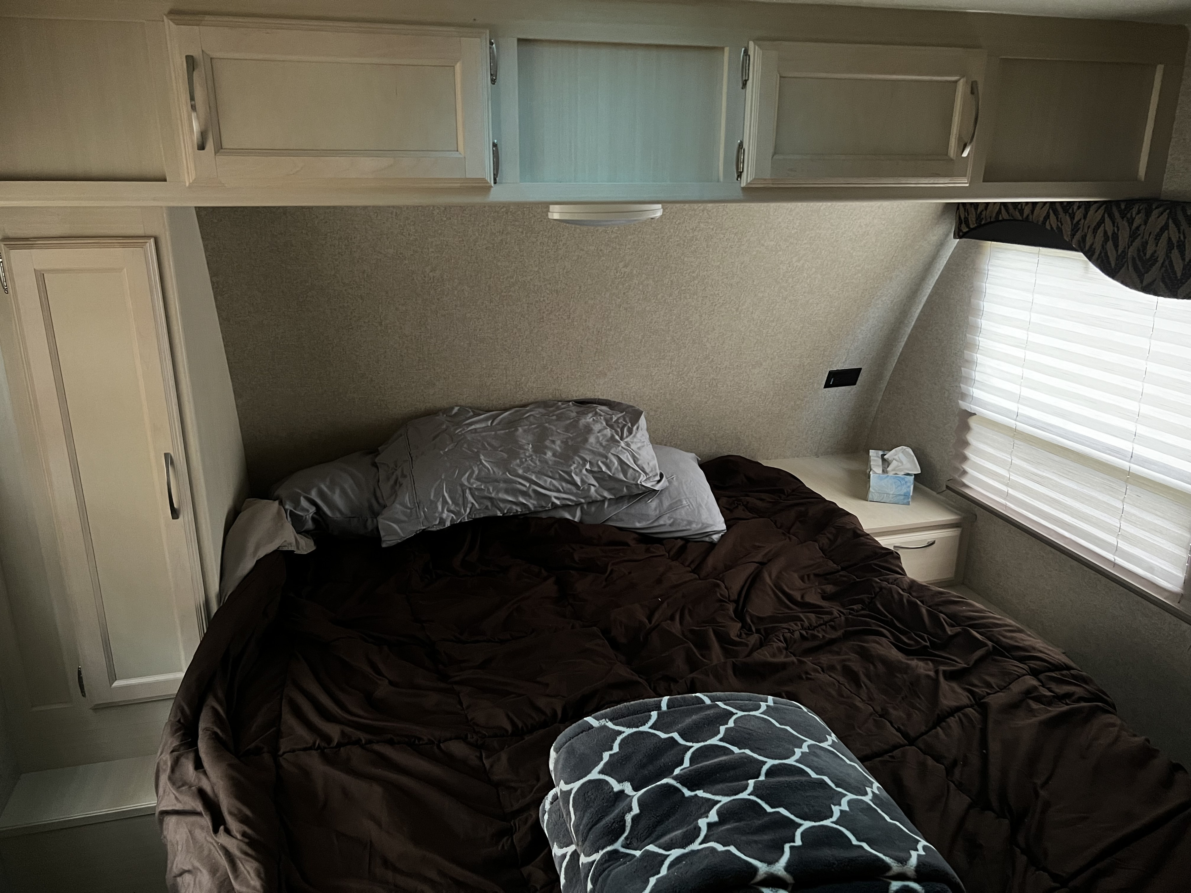 Inside an RV rental: a cozy bedroom with a comfortable bed, overhead cabinets, and window blinds.. Winnebago Minnie Winnie 2017