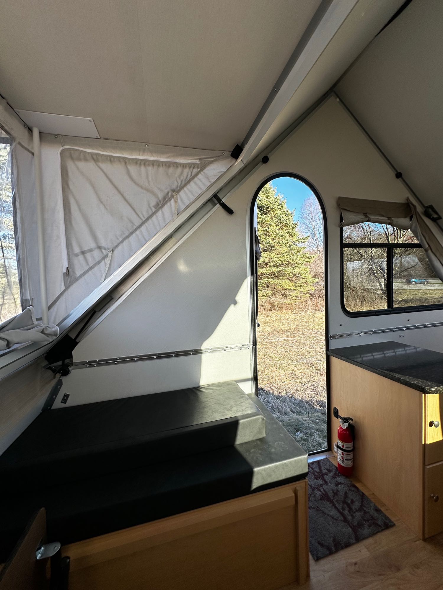 Inside a bright A-frame rv rental: comfy bed, compact kitchenette, and a door open to scenic outdoor views.. A Liner Ranger 12 2023