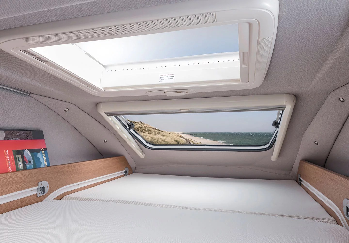 This RV rental's cozy sleeping area features a large skylight and a side window with a beautiful beach and ocean view.. weinsberg 600 MQH 2024