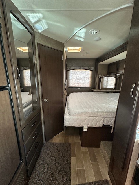 **RV rental** interior: A compact bedroom featuring a bed, dresser, window blinds, and access door.. Thor Chateau 2020