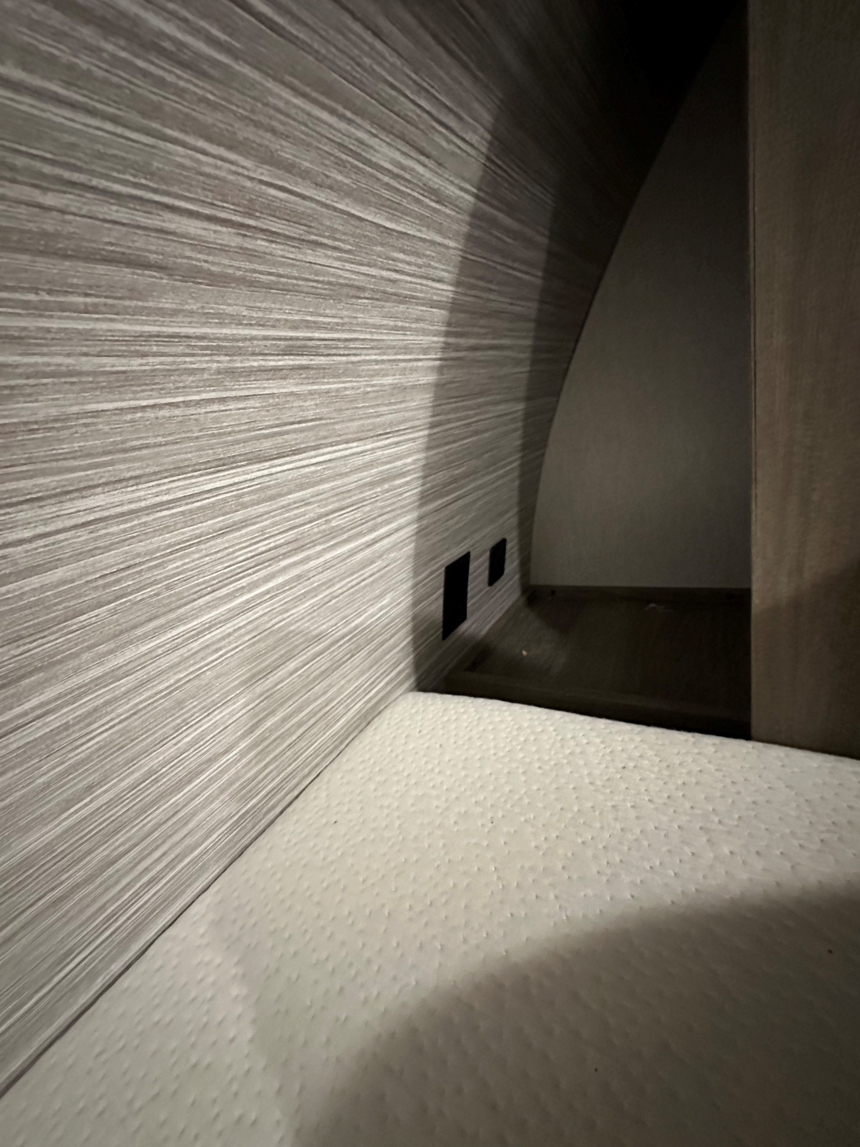 Cozy RV rental bunk features a modern wood-grain wall with charging ports, next to a comfortable textured mattress.. Forest River Wildwood Heritage Glen HL 2022