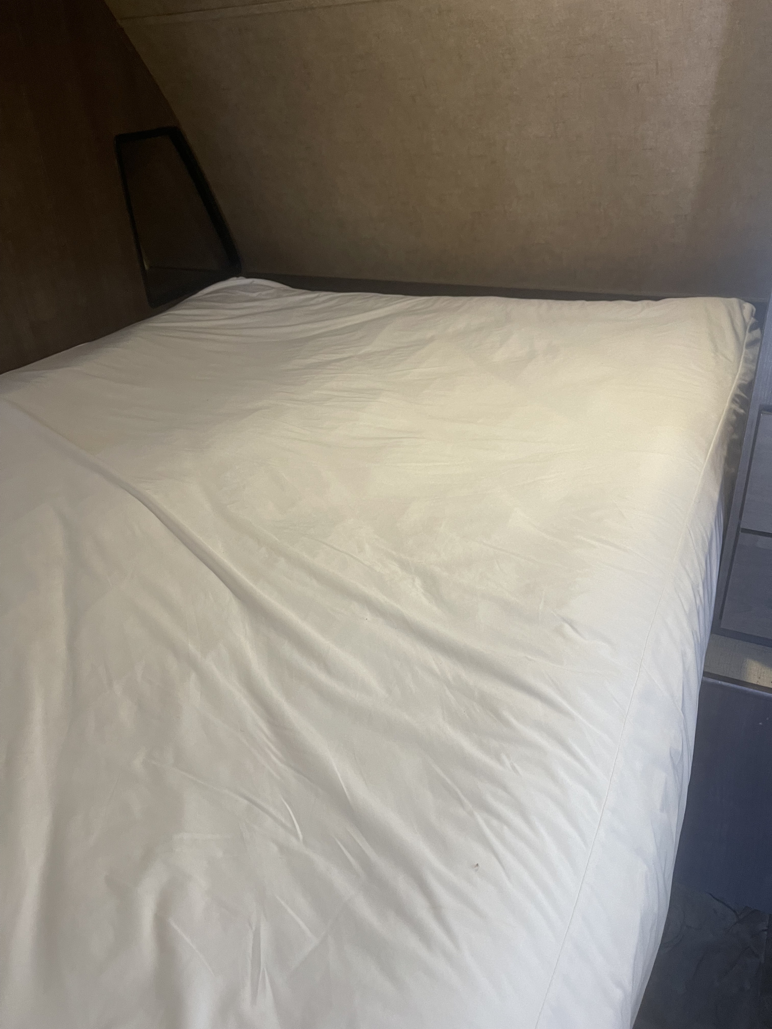 Clean bed inside an RV rental with white sheets and angled interior walls, ideal for travel.. Forest River Surveyor 2017
