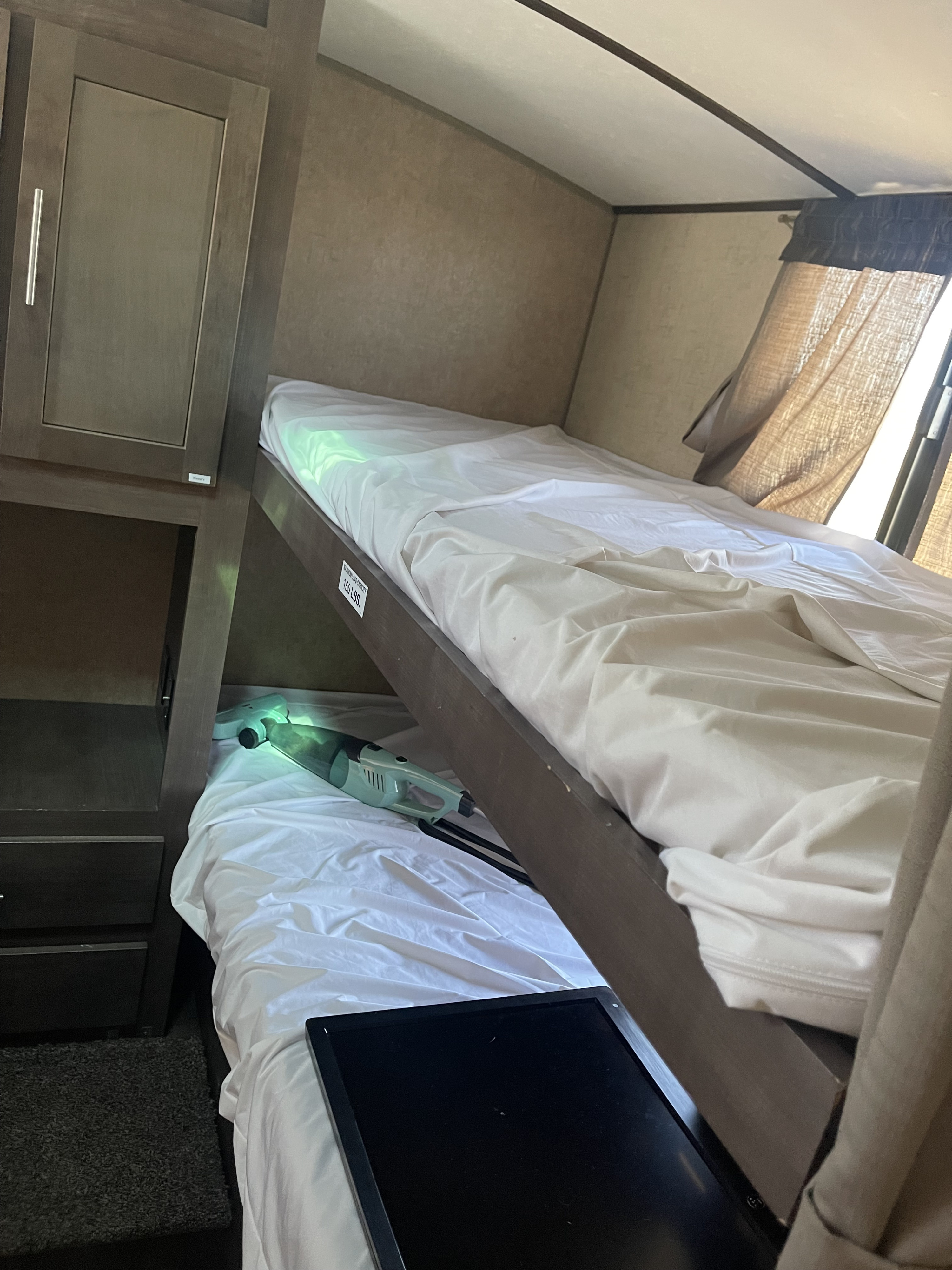 RV rental bunk beds with a cabinet, window, and cozy lower bunk featuring a vacuum and screen. Compact living essentials.. Forest River Surveyor 2017