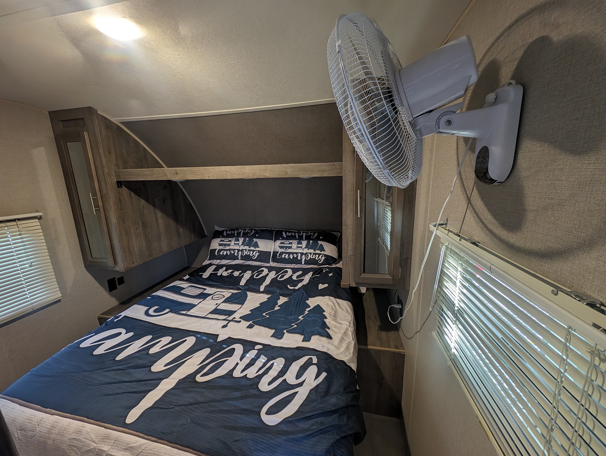Inside an RV rental: a compact bedroom with camping-themed bedding, wall-mounted fan, and windows with blinds.. Forest River Aurora Aurora 2021