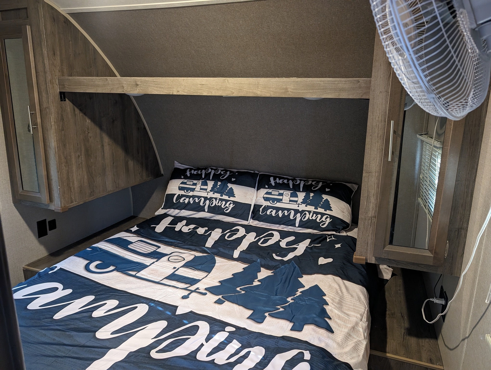 Cozy RV rental bedroom featuring "Happy Camping" bedding, overhead storage, and a fan, ready for adventure.. Forest River Aurora Aurora 2021