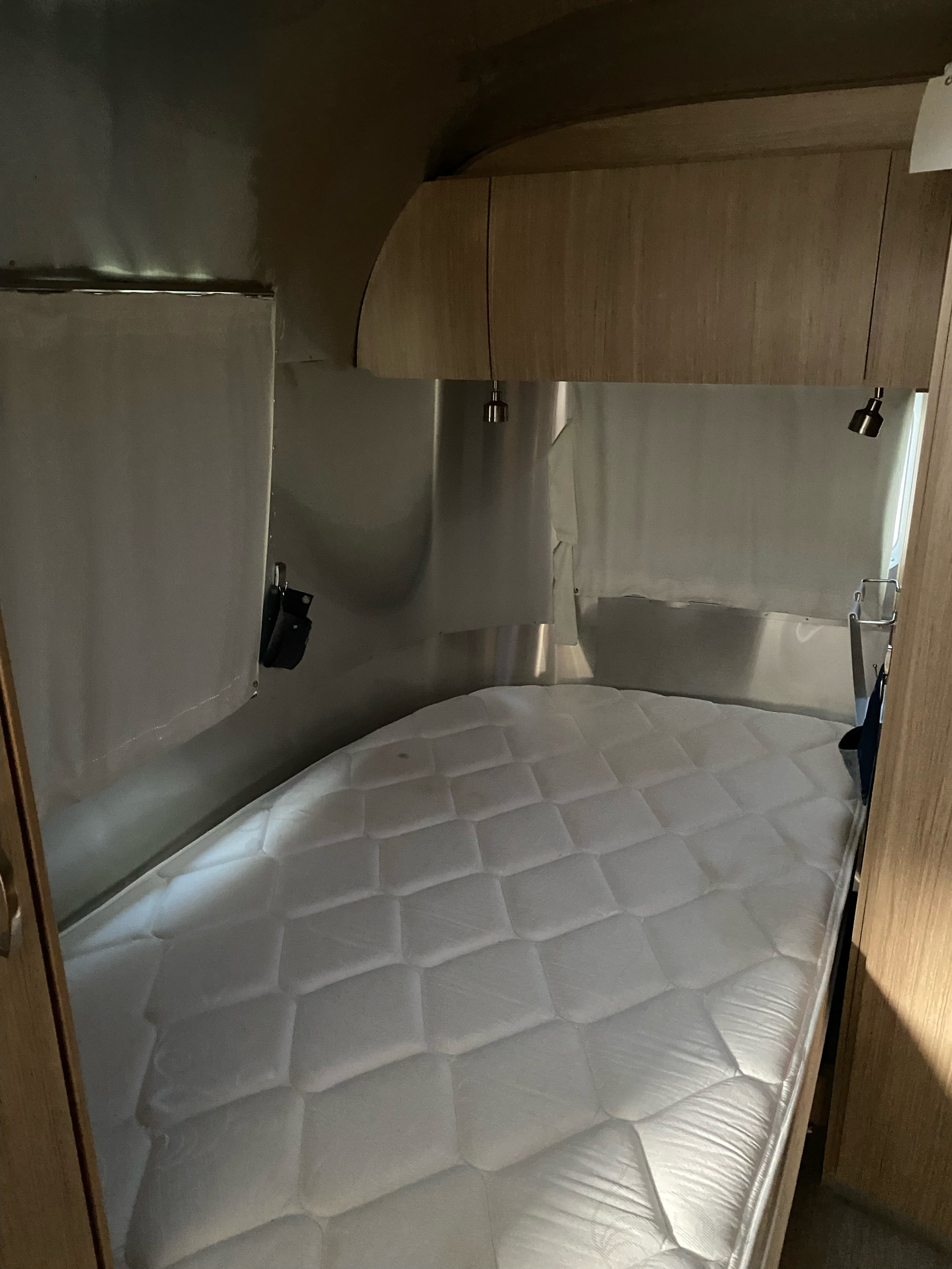 RV rental: Compact bedroom with a plush white mattress and modern wooden cabinetry inside a shiny metal-walled camper.. Airstream Flying Cloud 2018