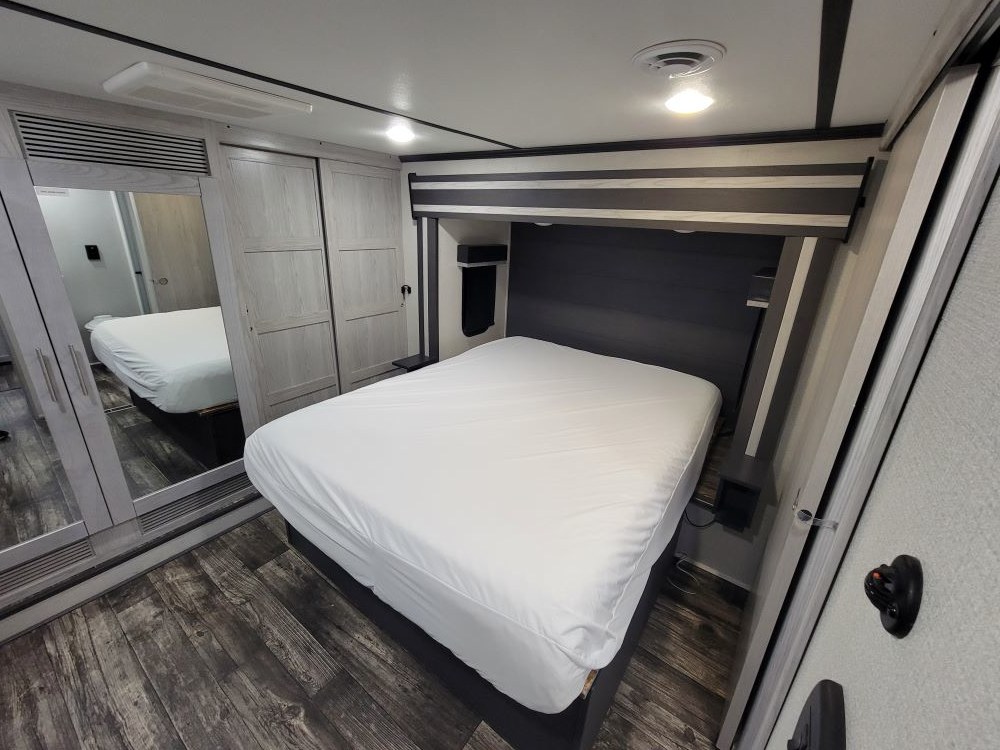 RV rental bedroom with a large bed, mirrored closet doors, wood-look floor, and built-in storage.. Keystone RV Fuzion Toy Hauler 2021
