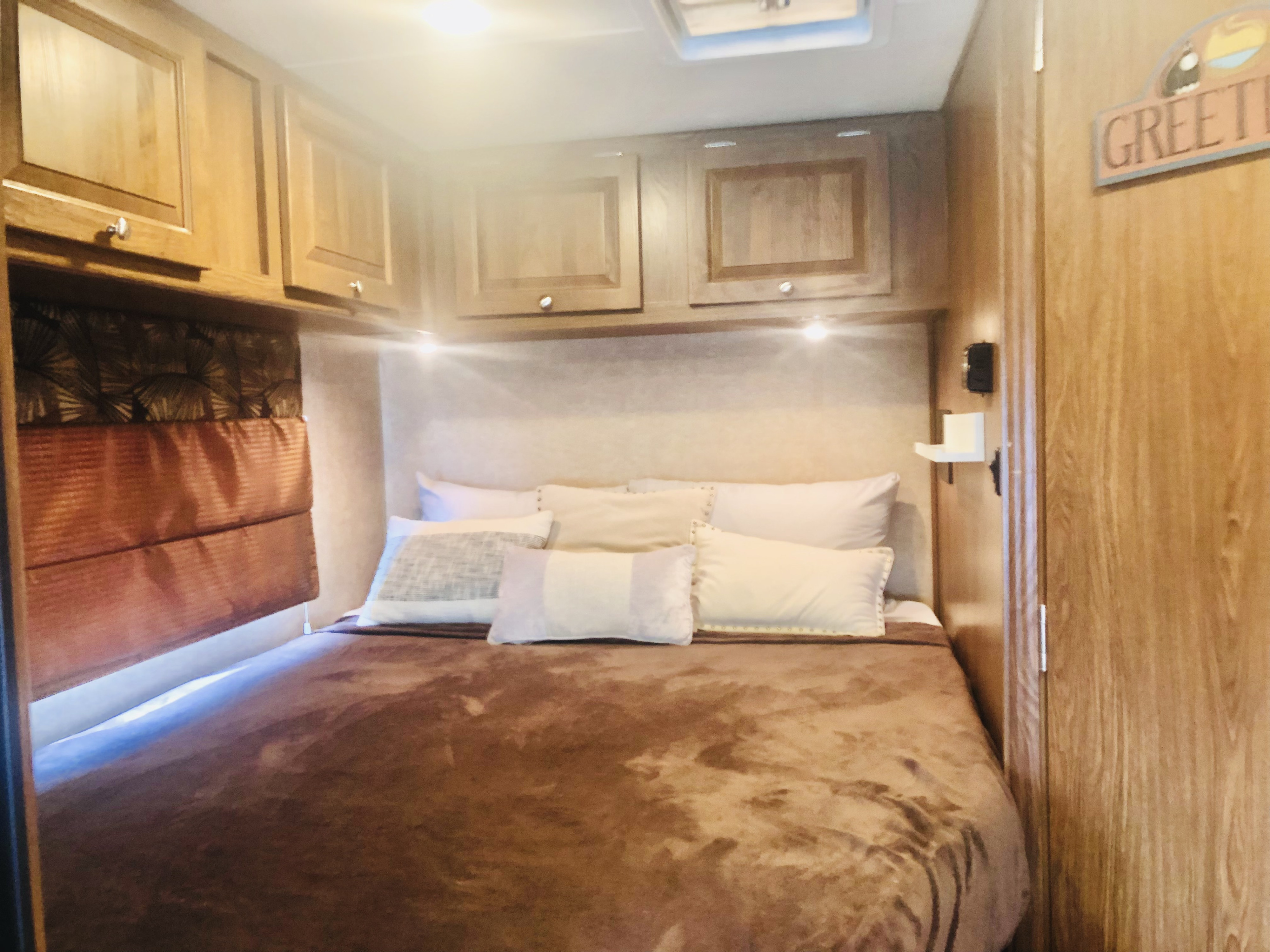Experience comfort in this RV rental bedroom: a plush bed with pillows, wooden overhead cabinets, and warm accent lighting.. Coachmen Leprechaun 2016