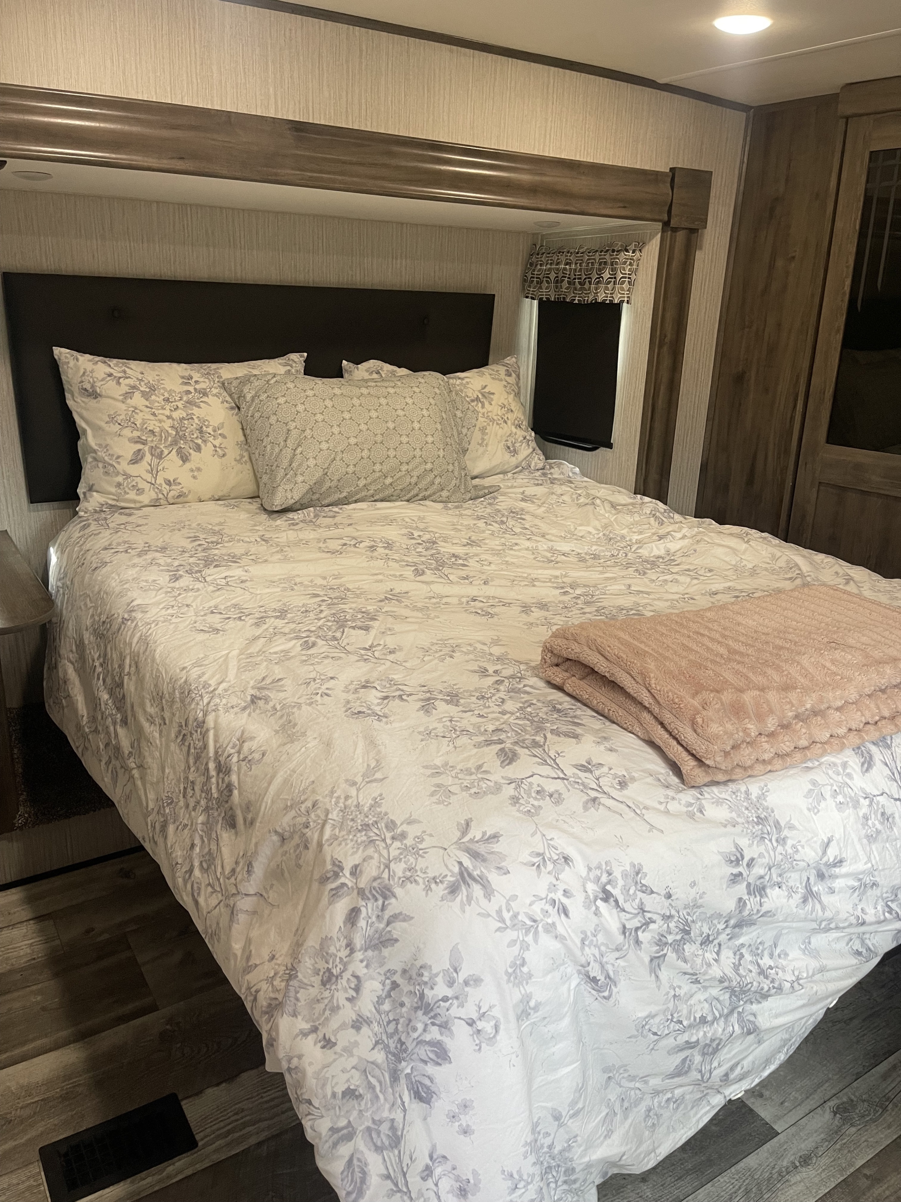 Cozy RV rental bedroom with a bed featuring white and grey floral bedding, plush pillows, and a soft pink blanket.. Forest River Sandpiper 2021