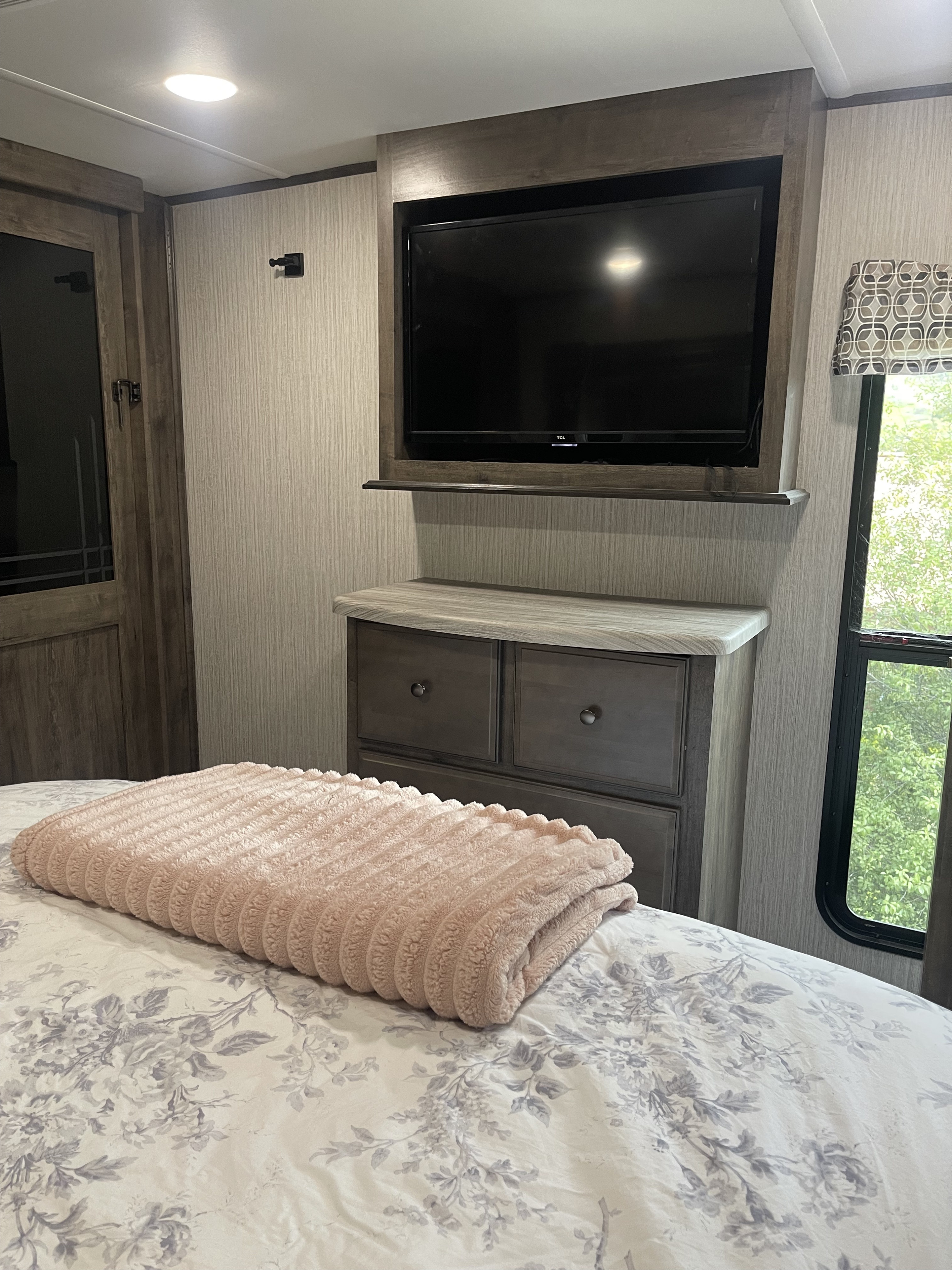 RV rental interior: A compact bedroom with a TV, dresser, and a cozy bed with pink throw and floral comforter.. Forest River Sandpiper 2021