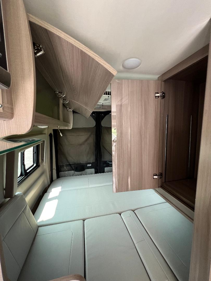 RV rental: Interior of a camper van featuring a comfortable reconfigurable bed, seating, and accessible overhead storage.. Thor Sequnce 2023