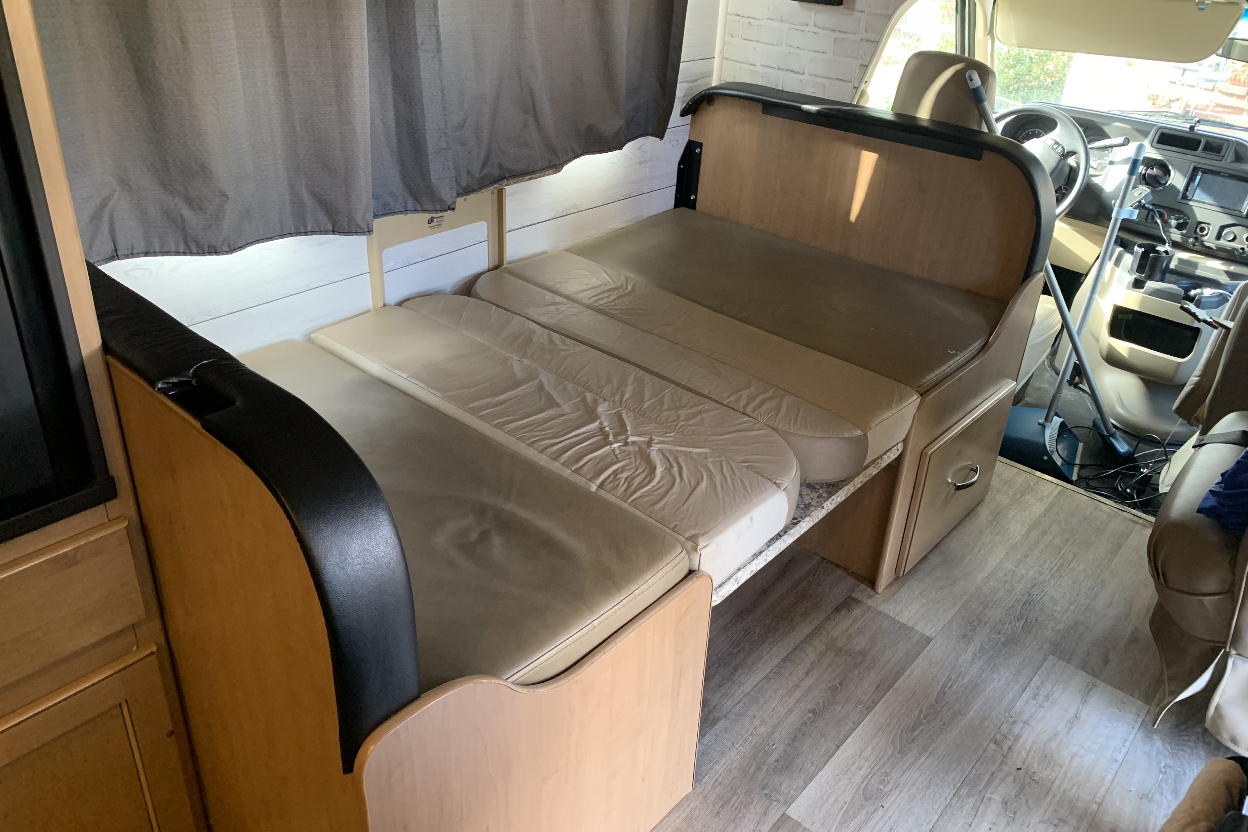 RV rental interior: A dinette area with light-colored cushions converted into a bed, featuring wooden cabinetry and the cockpit in the background.. Thor Four Winds 2020