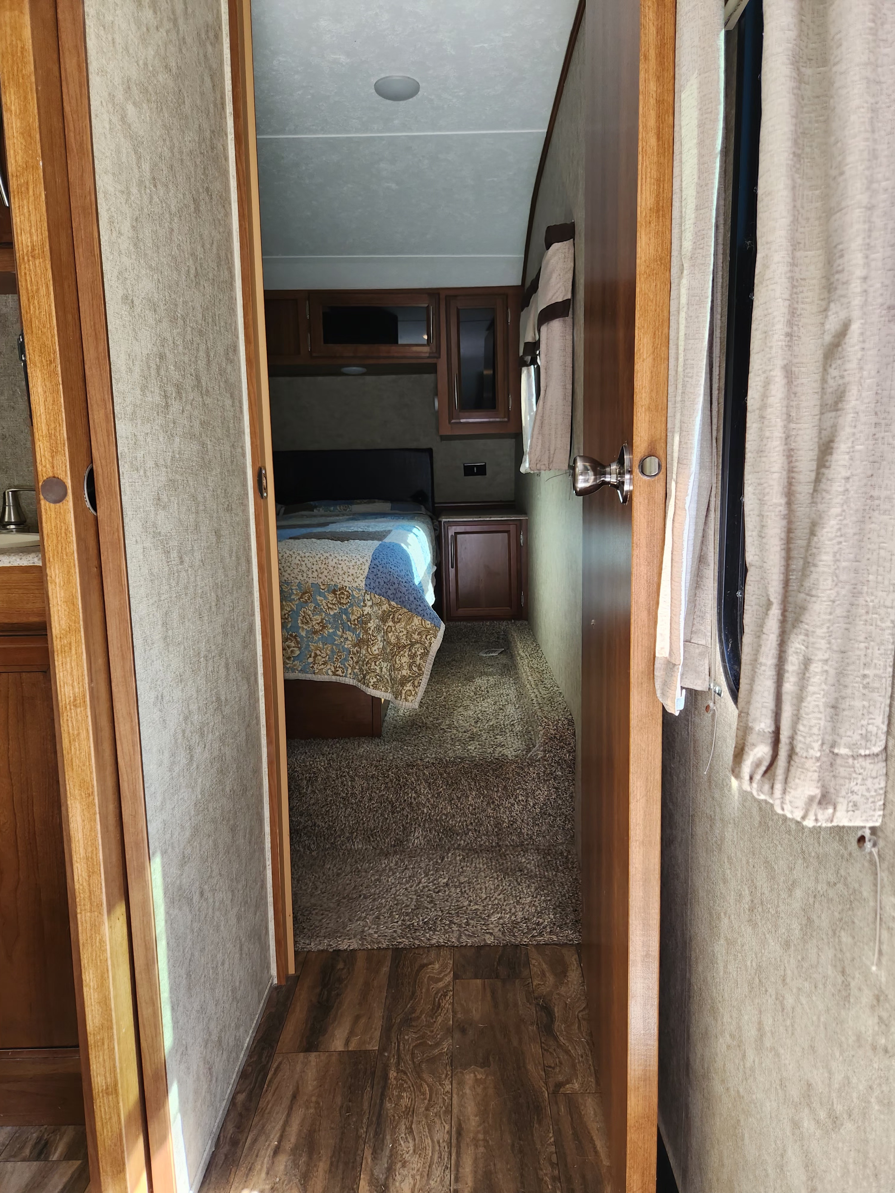 An RV rental's cozy interior, showing a bedroom with a patterned quilt and carpet, leading to a wood-floored hallway.. Crusader Crusader Fifth Wheel 2018