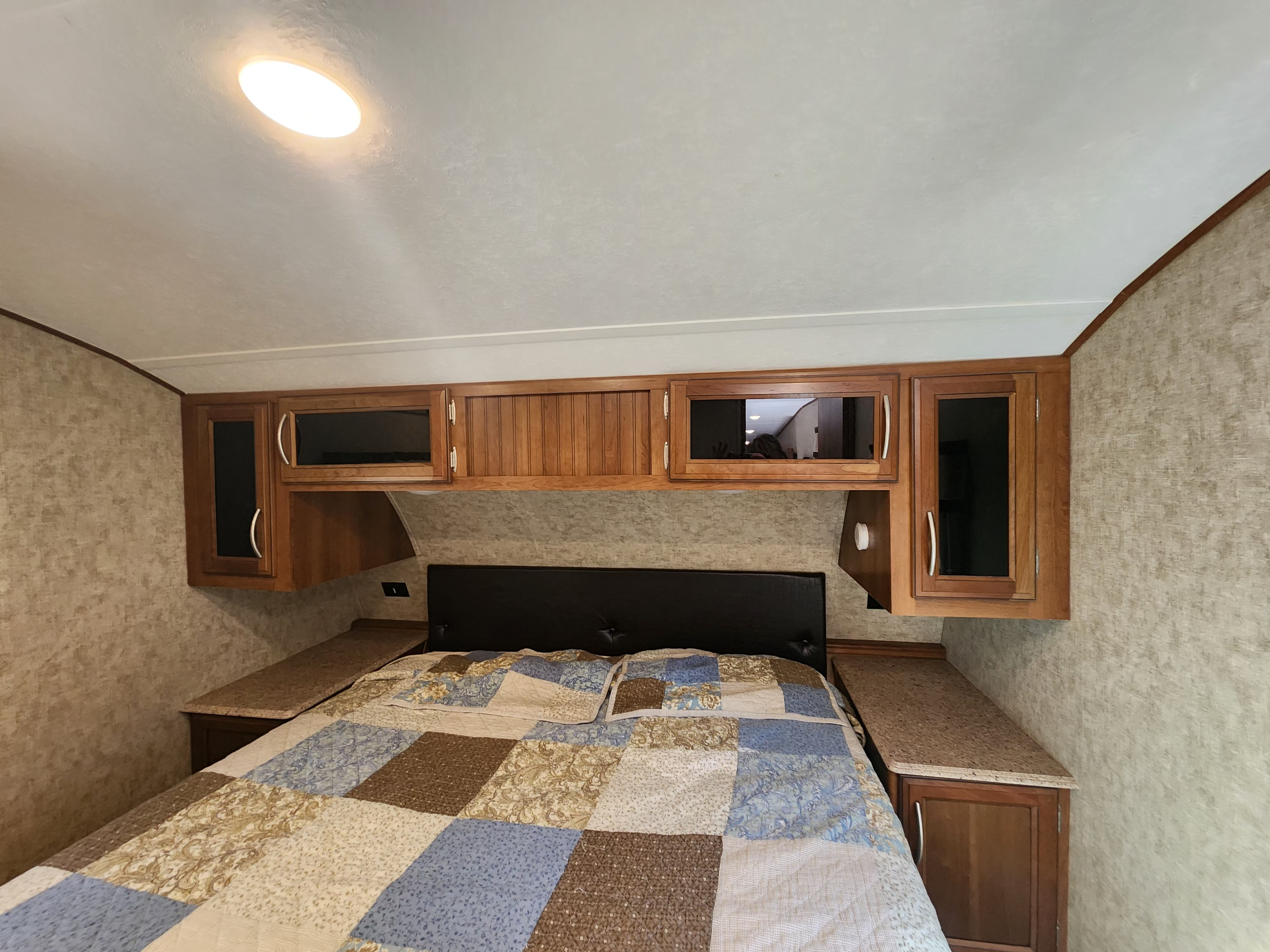 Cozy RV rental bedroom with a patchwork quilt on the bed, integrated wooden cabinets, and a bright ceiling light.. Crusader Crusader Fifth Wheel 2018