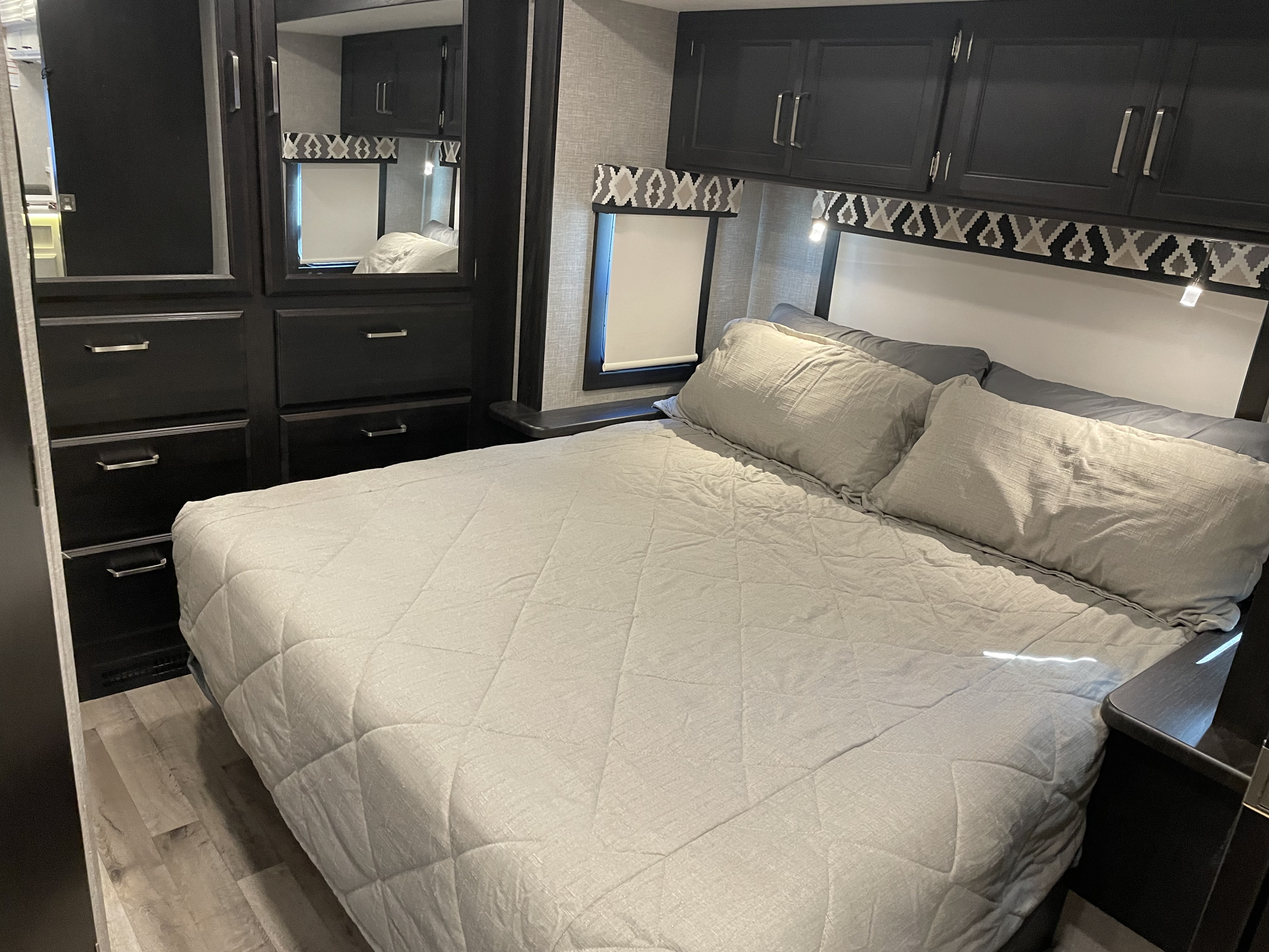 RV rental bedroom interior with light grey bedding, dark modern cabinets, and wood flooring. Ideal for a comfortable travel stay.. Jayco Alante 2021