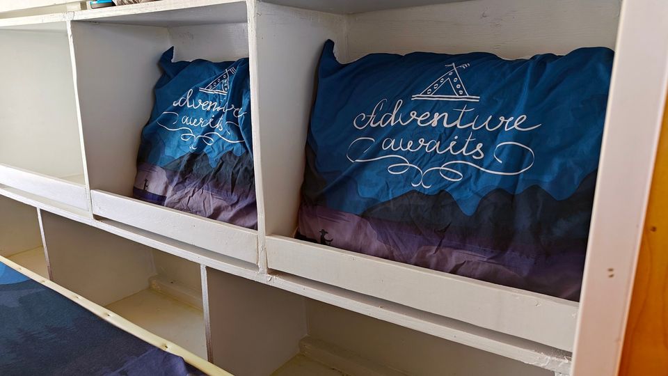RV rental bunk beds with "Adventure awaits" pillows and built-in storage cubbies, designed for compact living.. Mercedes-Benz Sprinter 2015