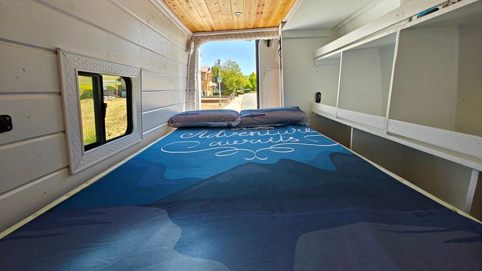 Adventure awaits in this cozy RV rental bed. Van interior with view of street, storage shelves, and a window.. Mercedes-Benz Sprinter 2015