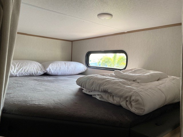 Inside an RV rental: a comfy bunk area with soft bedding, pillows, and a scenic window view.. Forest River Cherokee Alpha Wolf 2024