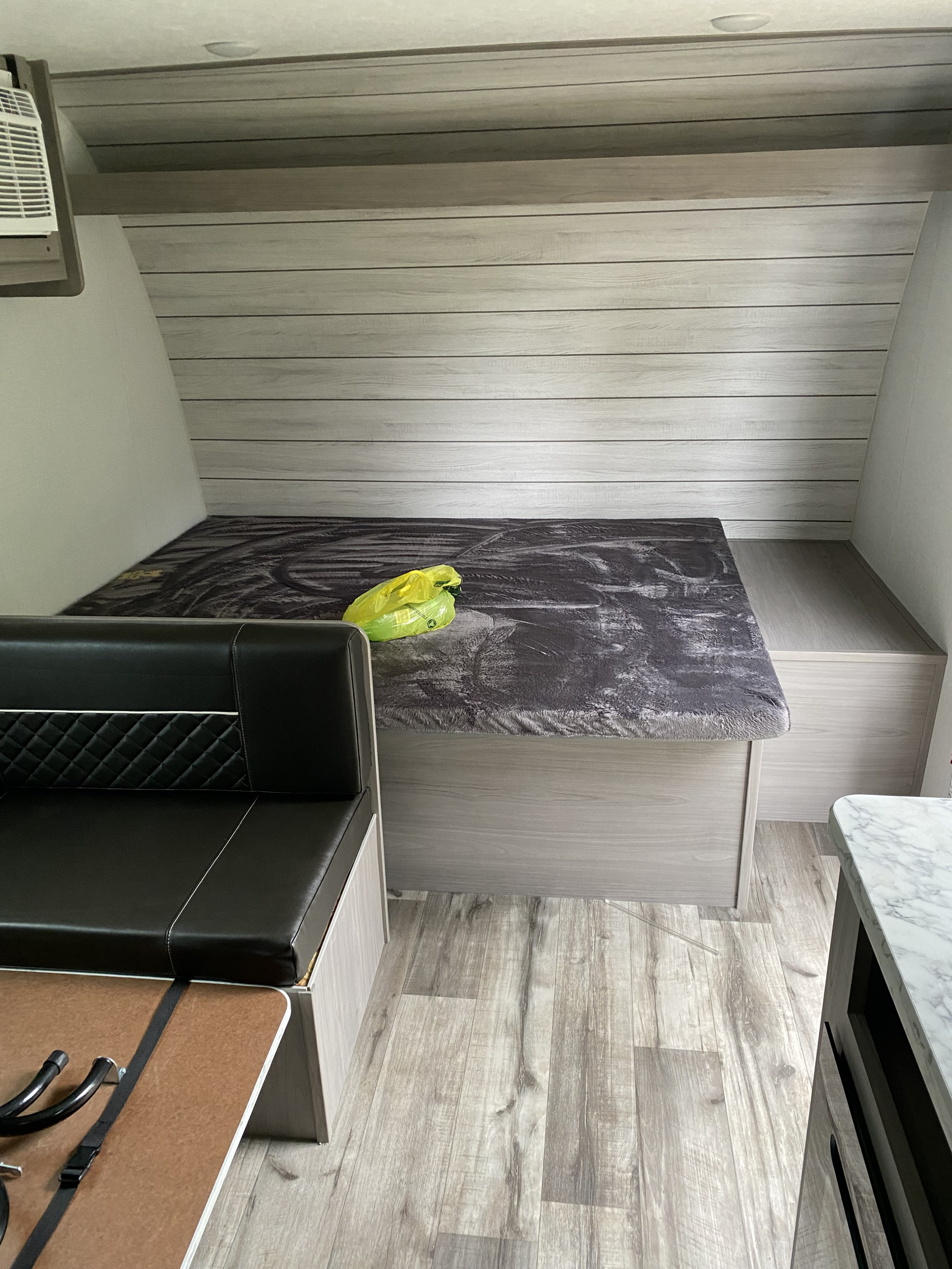 An RV rental features a cozy bed with a dark grey blanket, black leather dinette, and light wood-look interior.. Keystone RV Coleman lantern 17b 2024