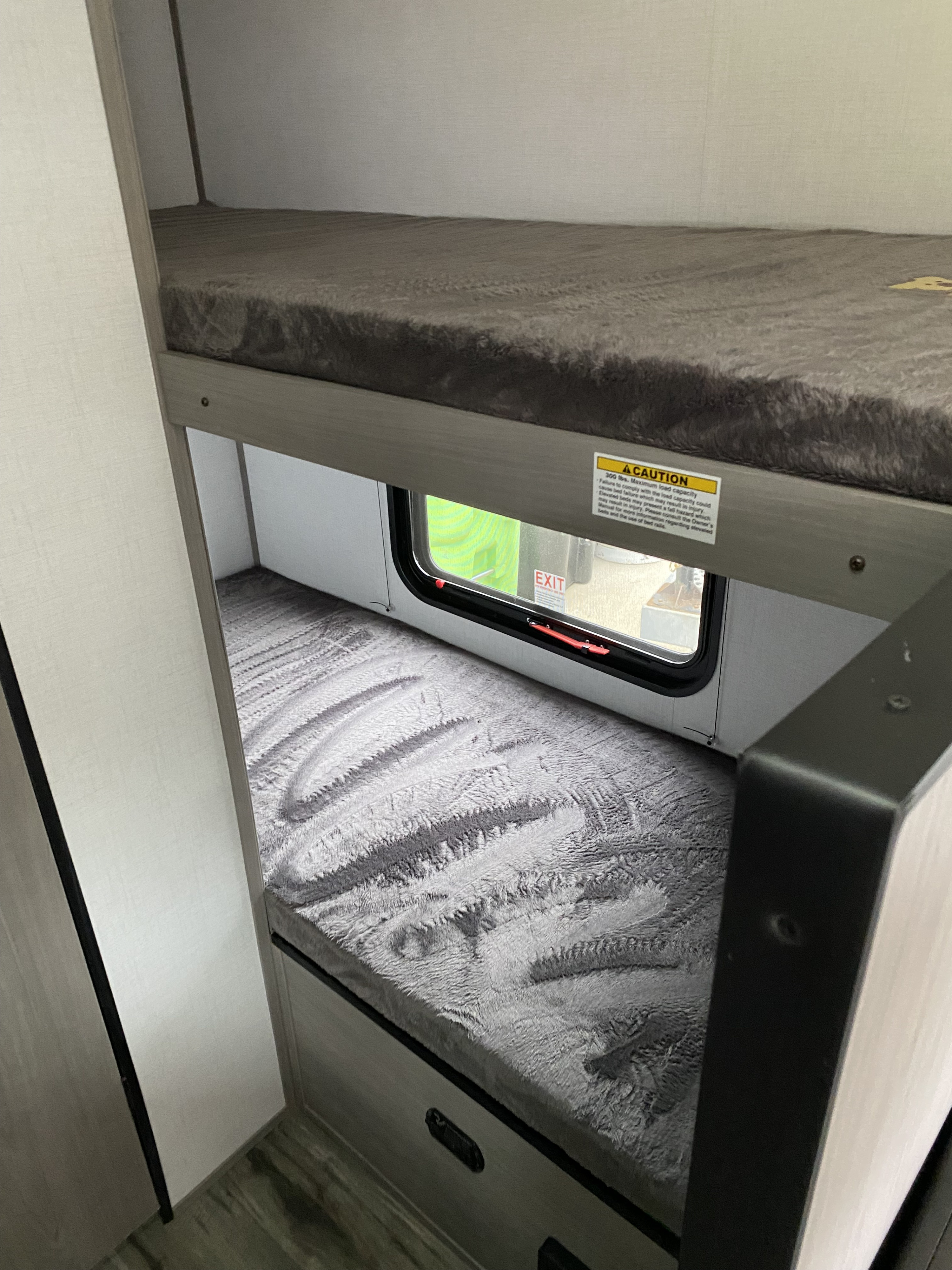 RV rental's cozy bunk beds with fuzzy grey mattress pads and an emergency exit window.. Keystone RV Coleman lantern 17b 2024