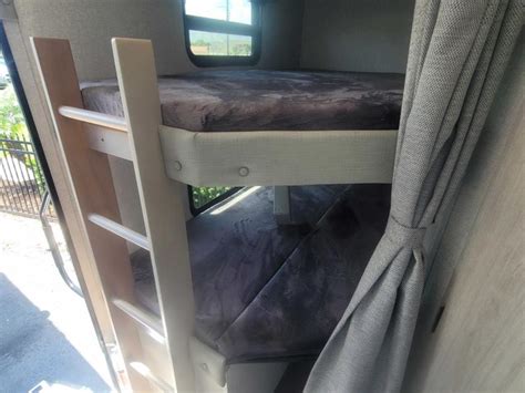 RV rental bunk beds, with a ladder for the top bunk & a tied-back curtain, offer cozy sleeping space inside.. East to West Alta 2022