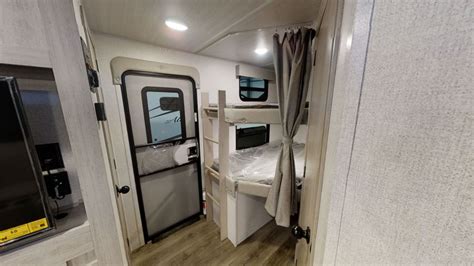 RV rental interior. View of compact bunk beds with privacy curtains, a small window, and an entry door. Beds are plastic-covered.. East to West Alta 2022
