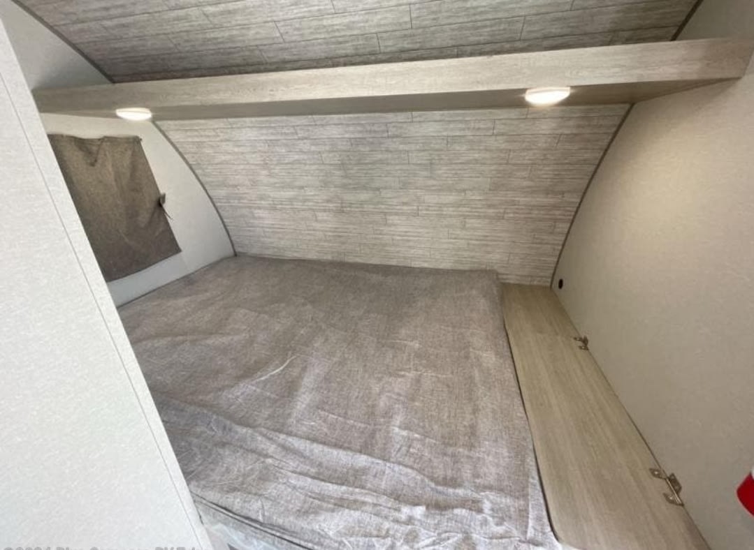 RV rental bedroom: cozy space with large bed, window, overhead shelf with lights, and wood-look paneling.. Forest River Aurora Aurora Light 2024