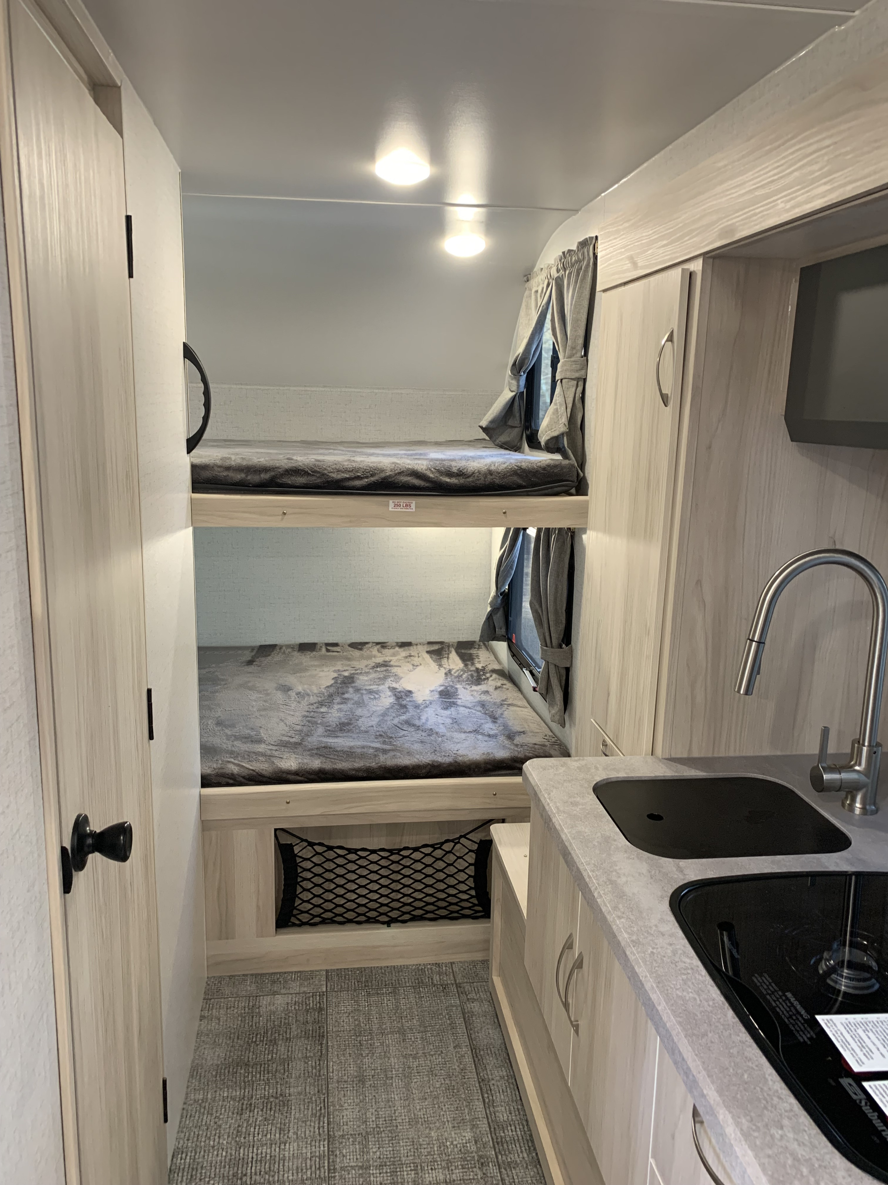 View of an RV rental interior showcasing practical bunk beds and a compact kitchen counter with sink.. Winnebago Hike 2022