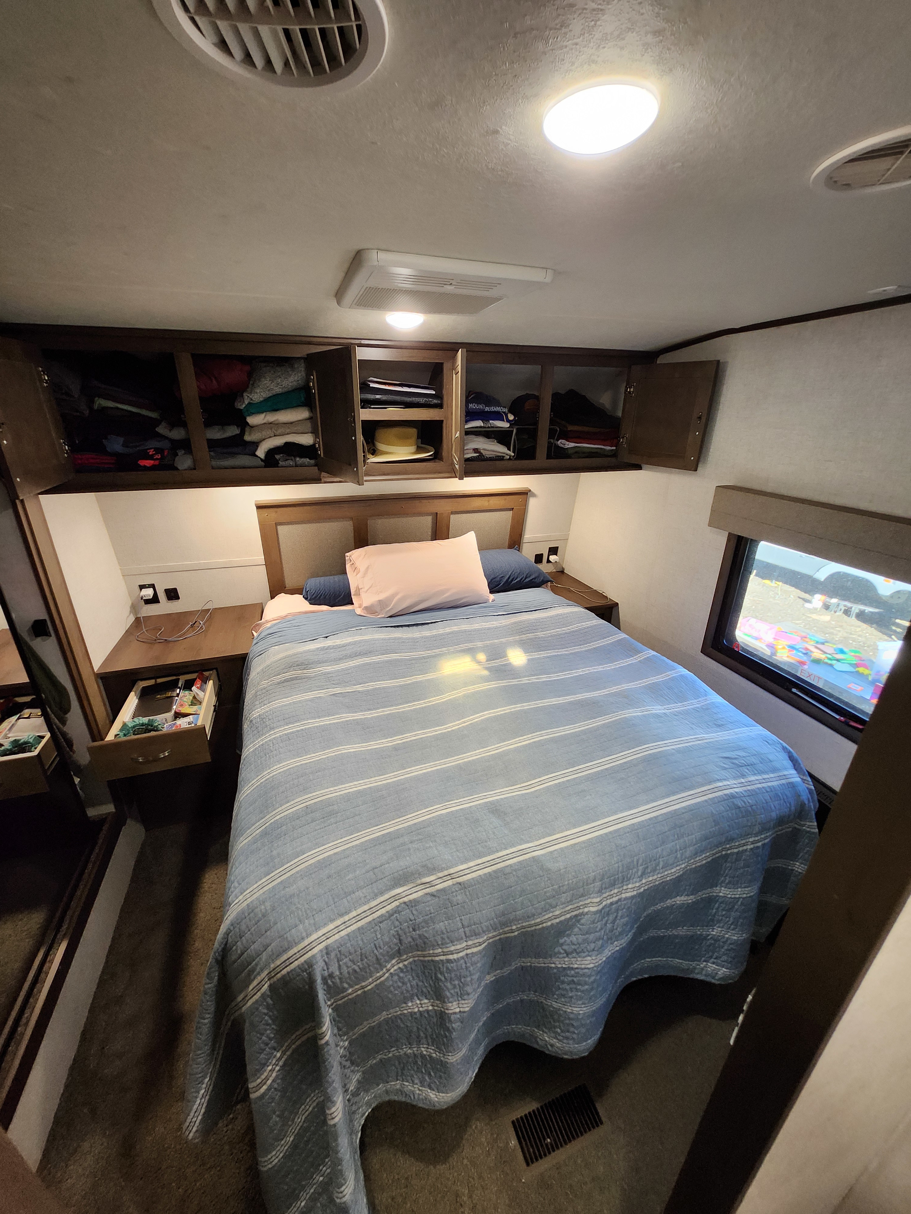 RV rental bedroom interior: Features overhead storage, a striped bed, and bedside tables with power outlets.. Highland Ridge RV Open Range 2019