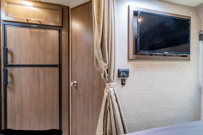 RV rental: Dometic fridge, door, privacy curtain, wall-mounted TV, & climate control unit. Cozy travel interior.. Thor Four Winds 2021