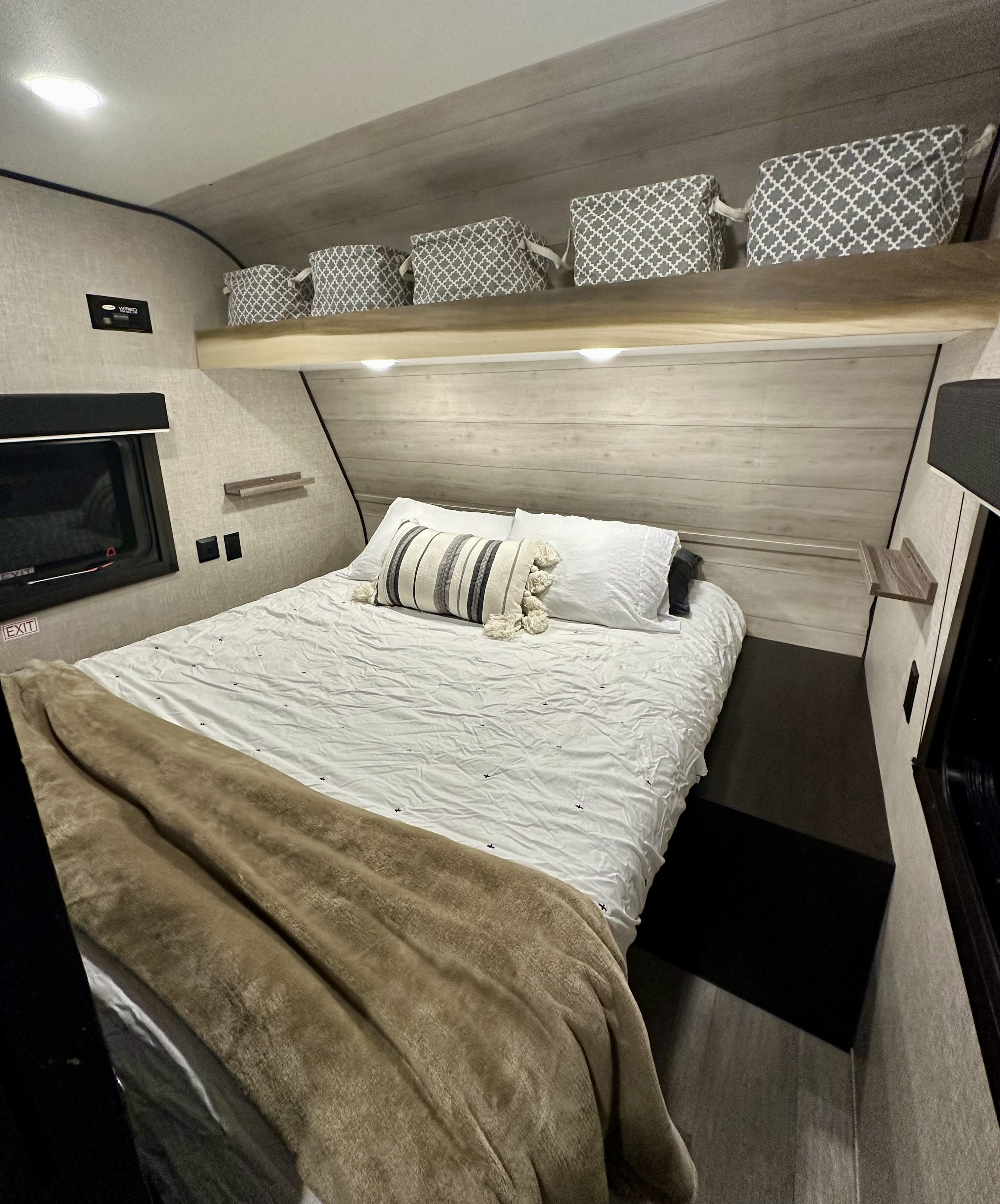 Cozy RV rental bedroom featuring a bed with white bedding, overhead storage baskets, and built-in lighting for a comfortable stay.. Jayco Jay Flight SLX 2022