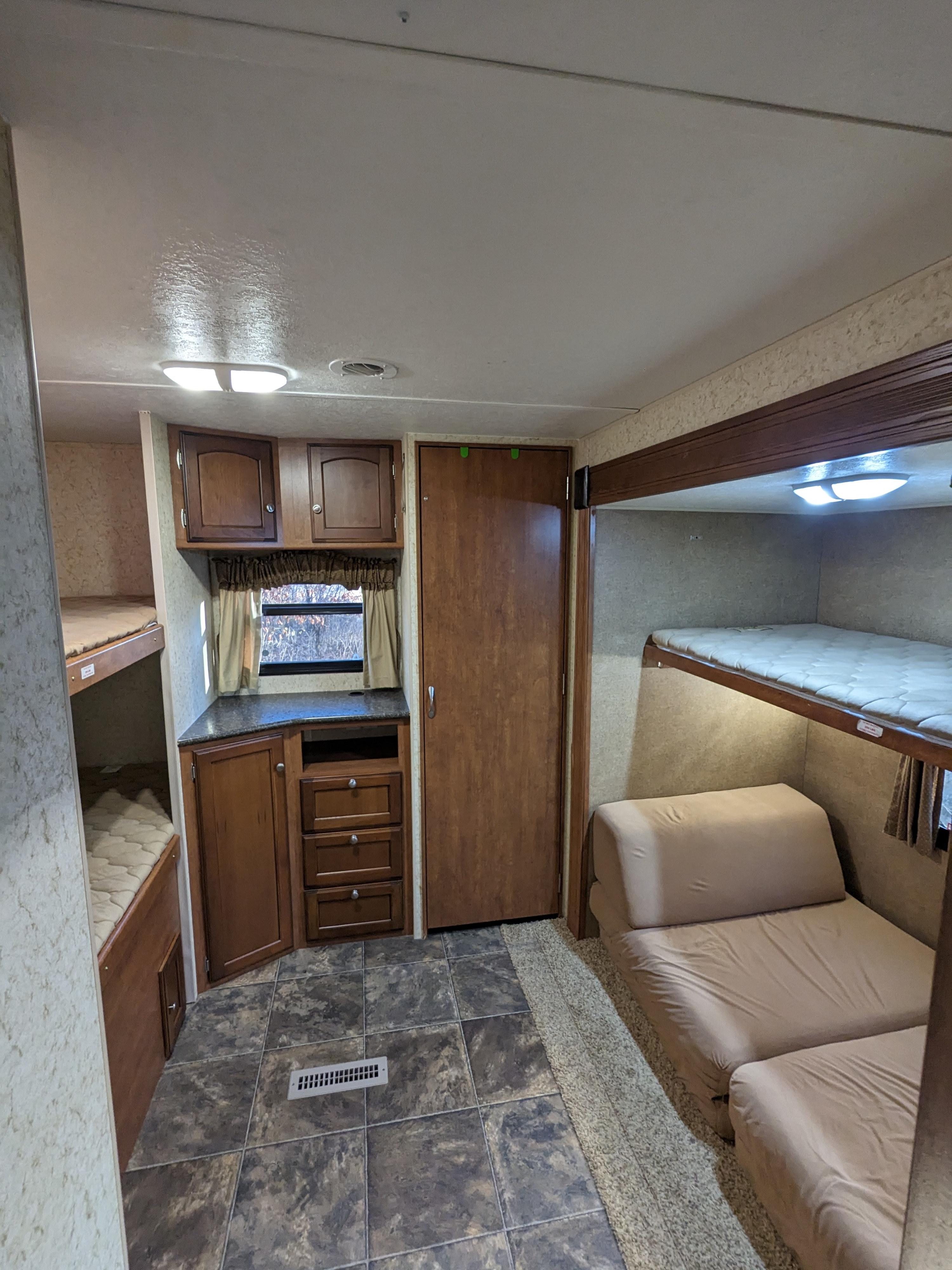 This RV rental interior shows a compact bunkhouse area with three beds, a fold-out sofa, and wood-look cabinetry.. Winnebago Sunset Creek 2014